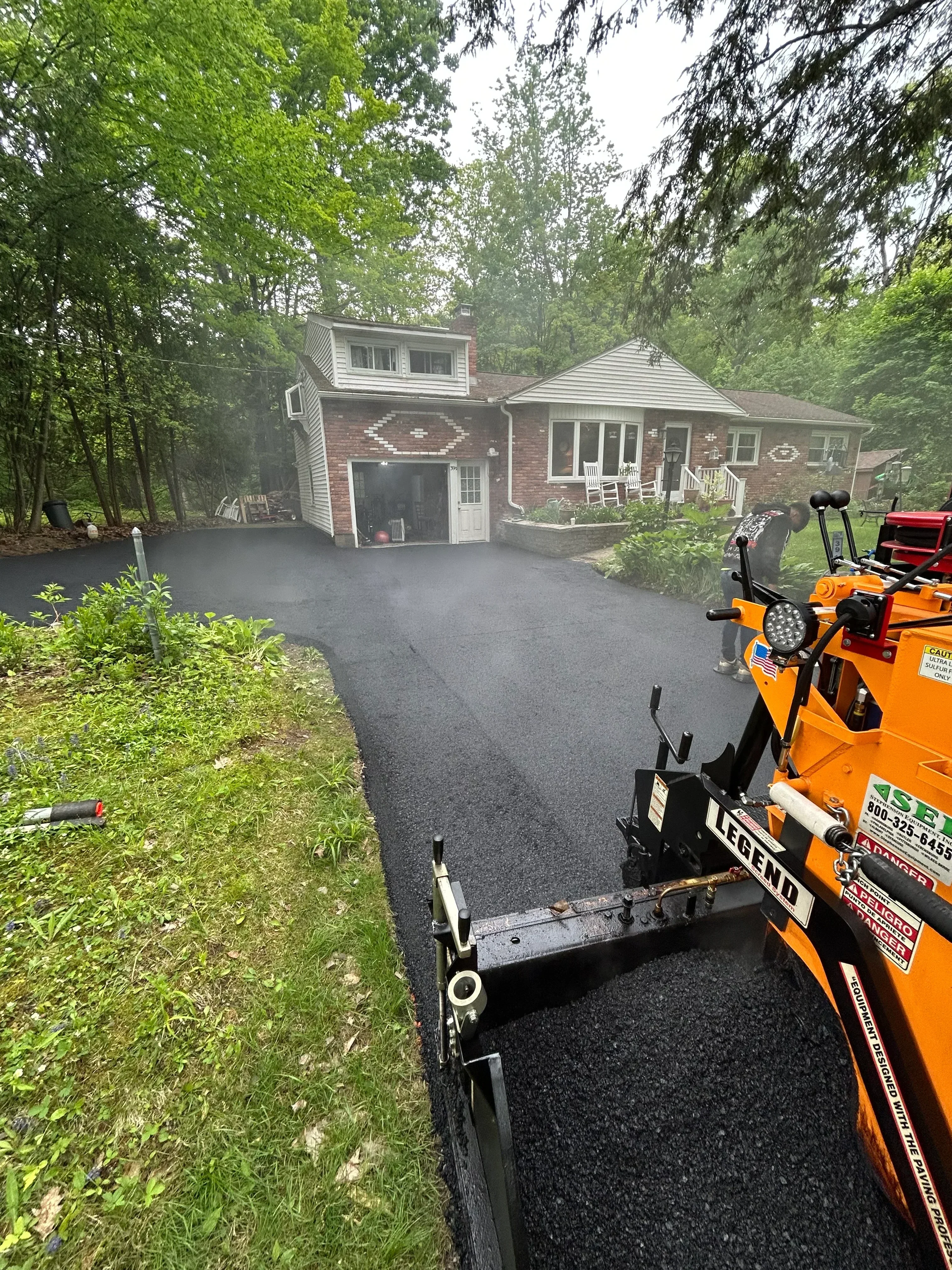 Newly installed black asphalt driveway with paving truck and equipment on-site