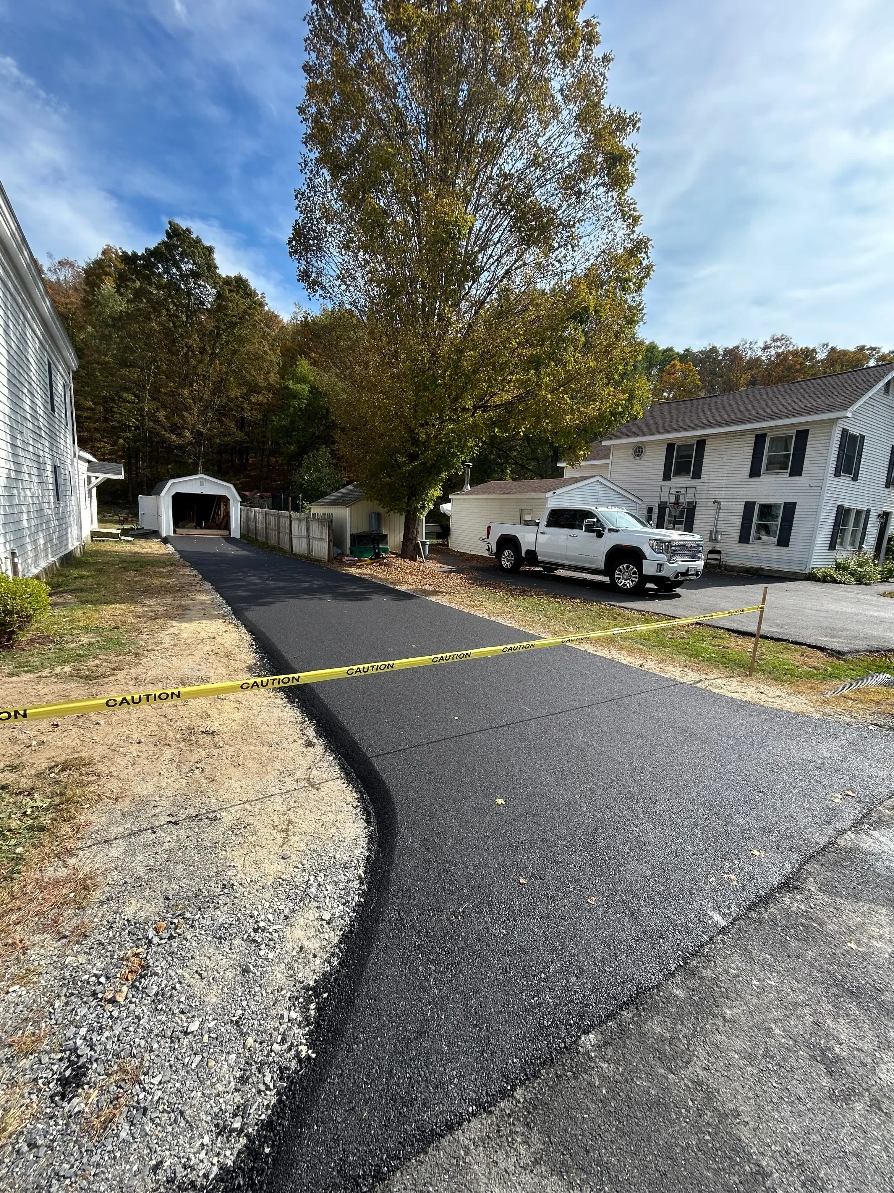 New asphalt driveway with yellow caution tape, residential home in background