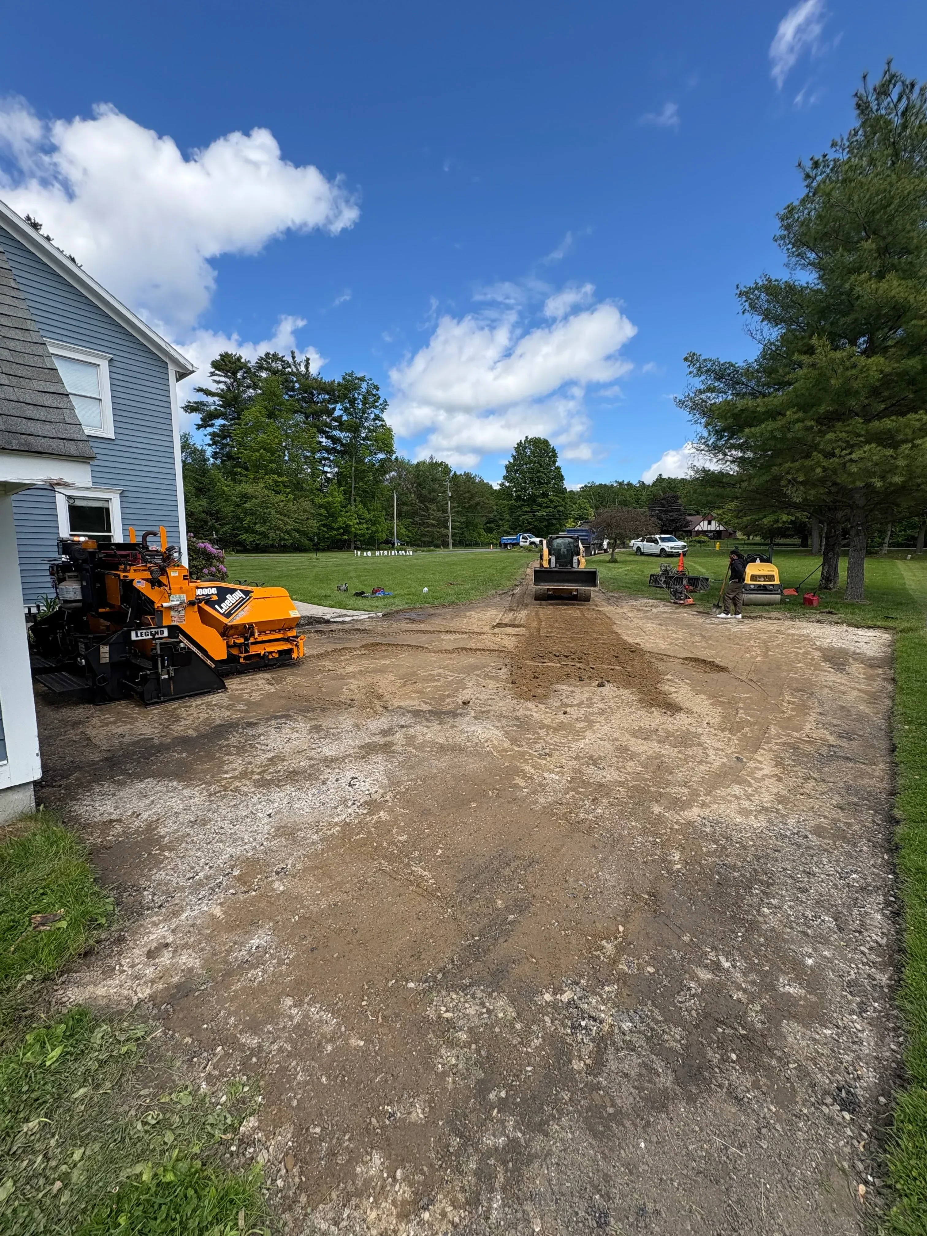 Orange asphalt paver laying fresh asphalt on residential driveway with gravel base