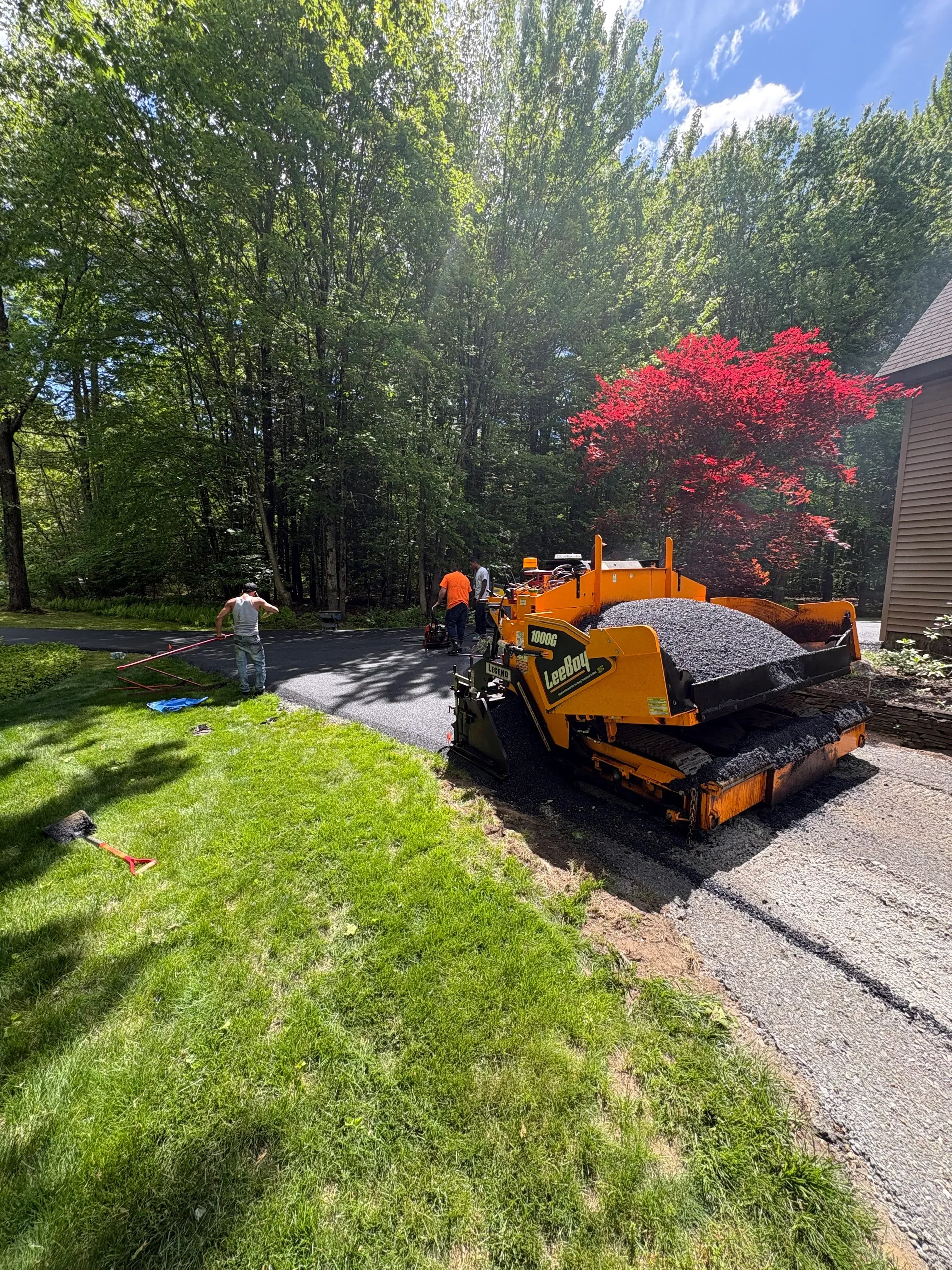 Yellow asphalt milling machine removing pavement from driveway with collected material visible