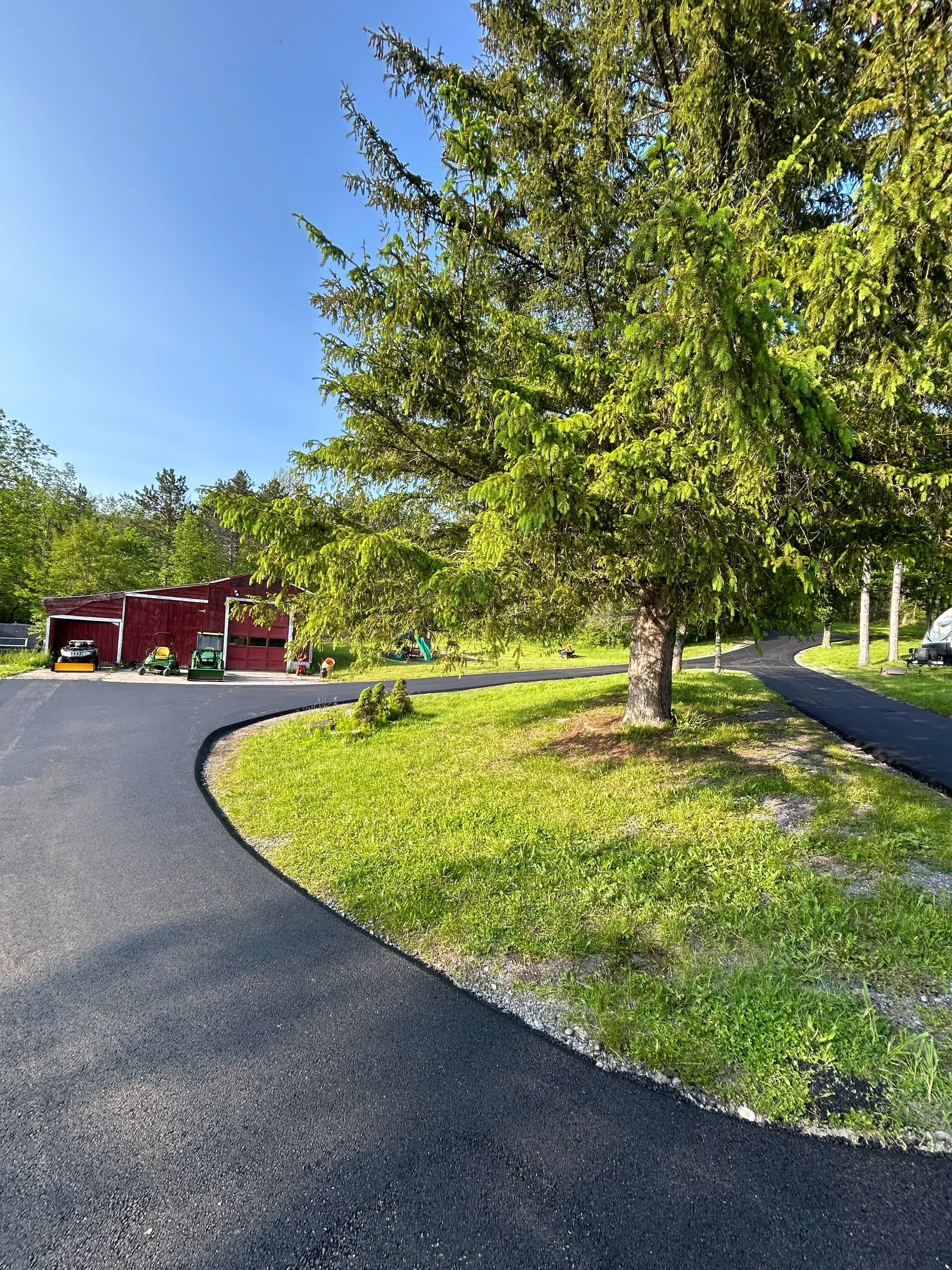 Newly paved asphalt driveway with curved edge detail and established lawn borders