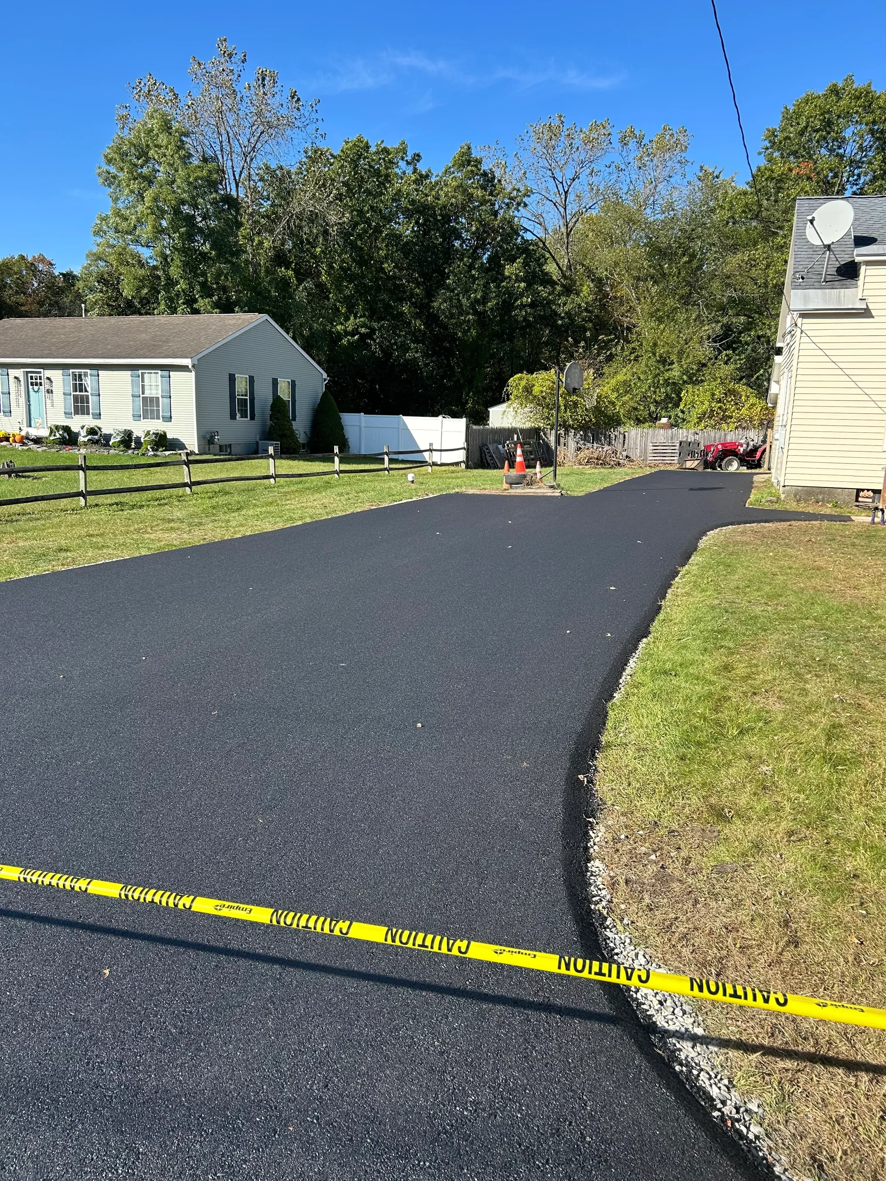 New black asphalt driveway with white edge lines and gravel borders along residential property