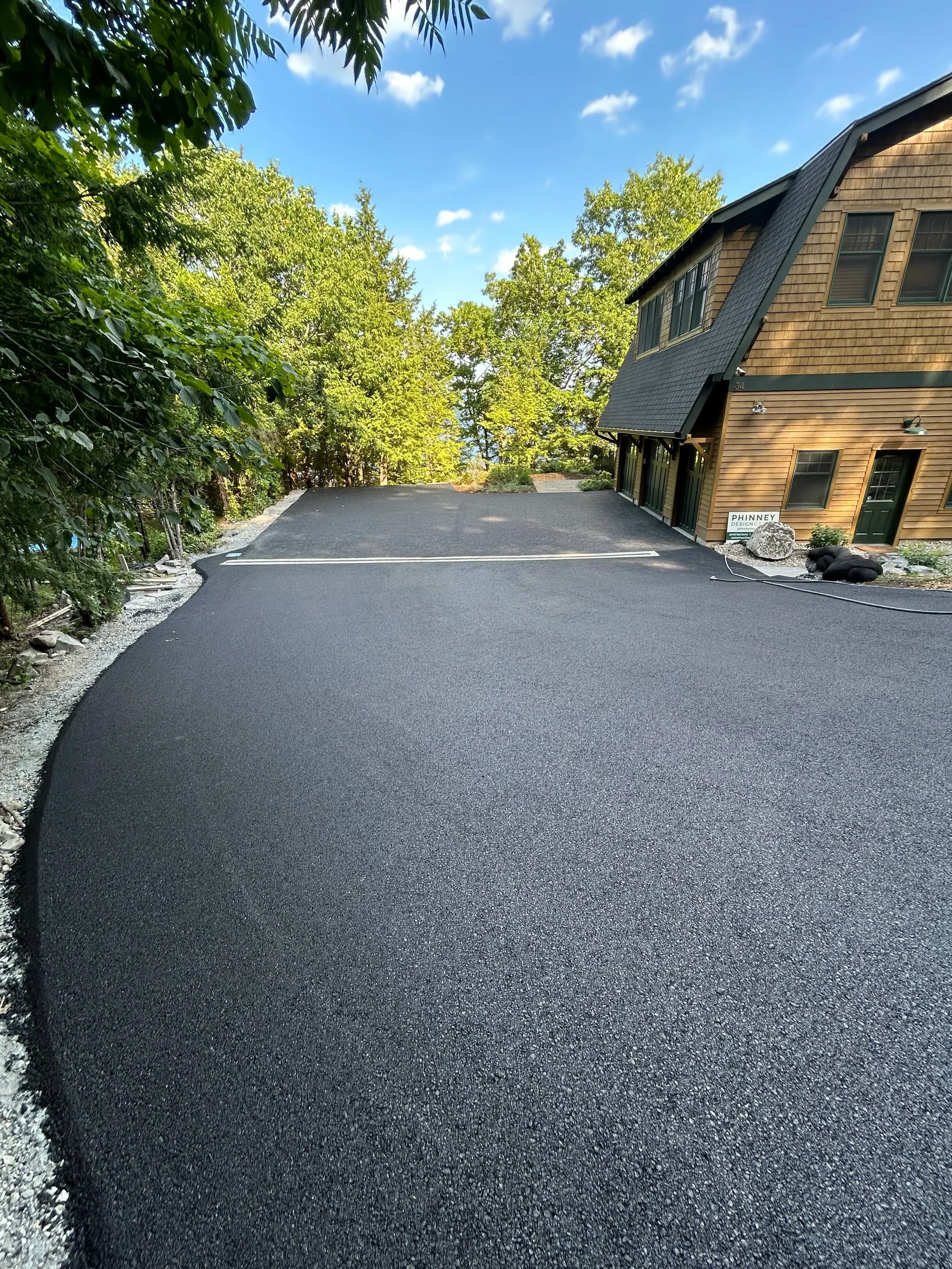 New dark asphalt driveway next to brick home with metal roof and gravel edge