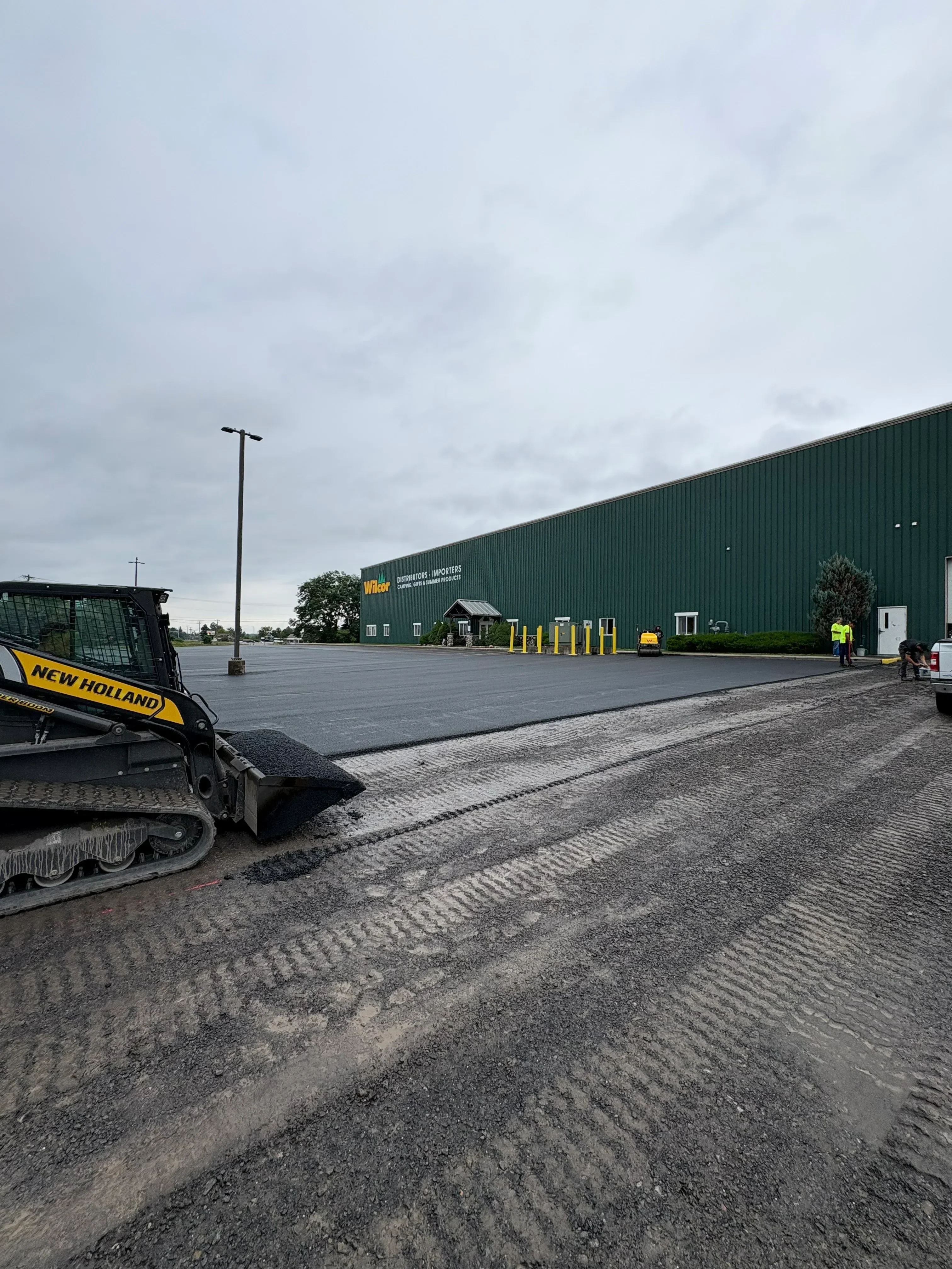 Fresh asphalt driveway with compacted surface and equipment on commercial property