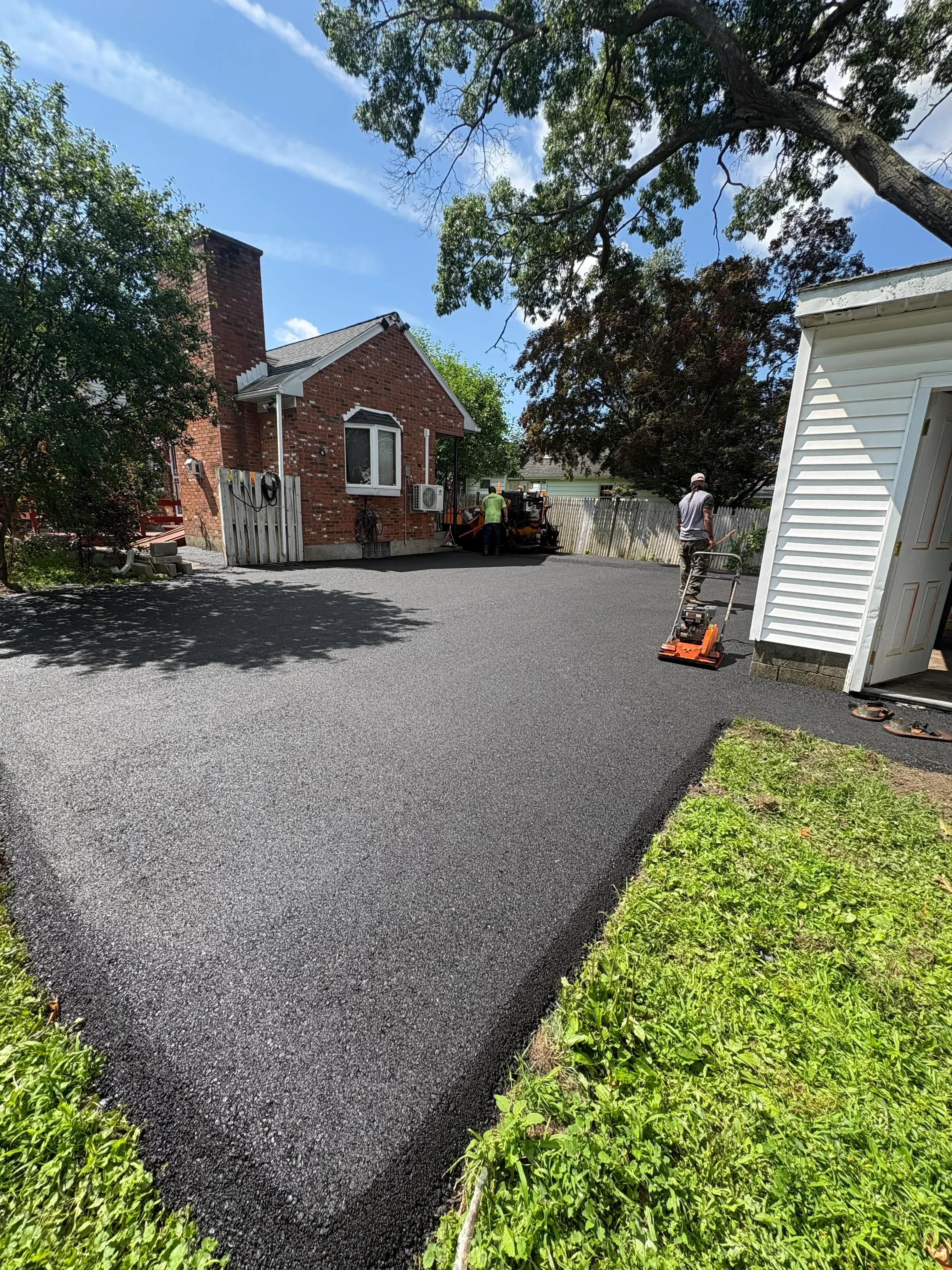 New asphalt driveway with brick residential home and manicured hedges