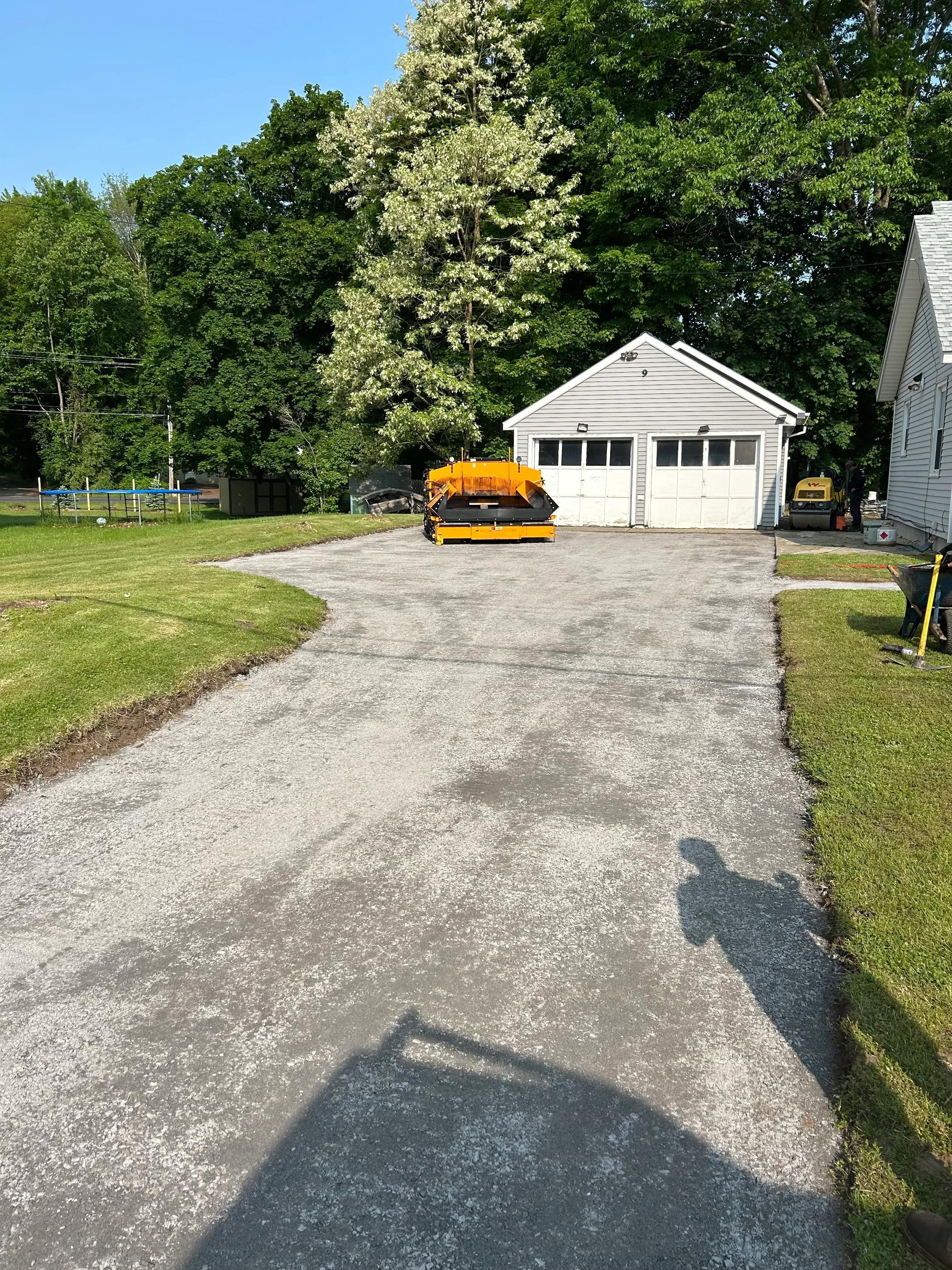 Newly installed dark asphalt driveway beside white residential home with green lawn