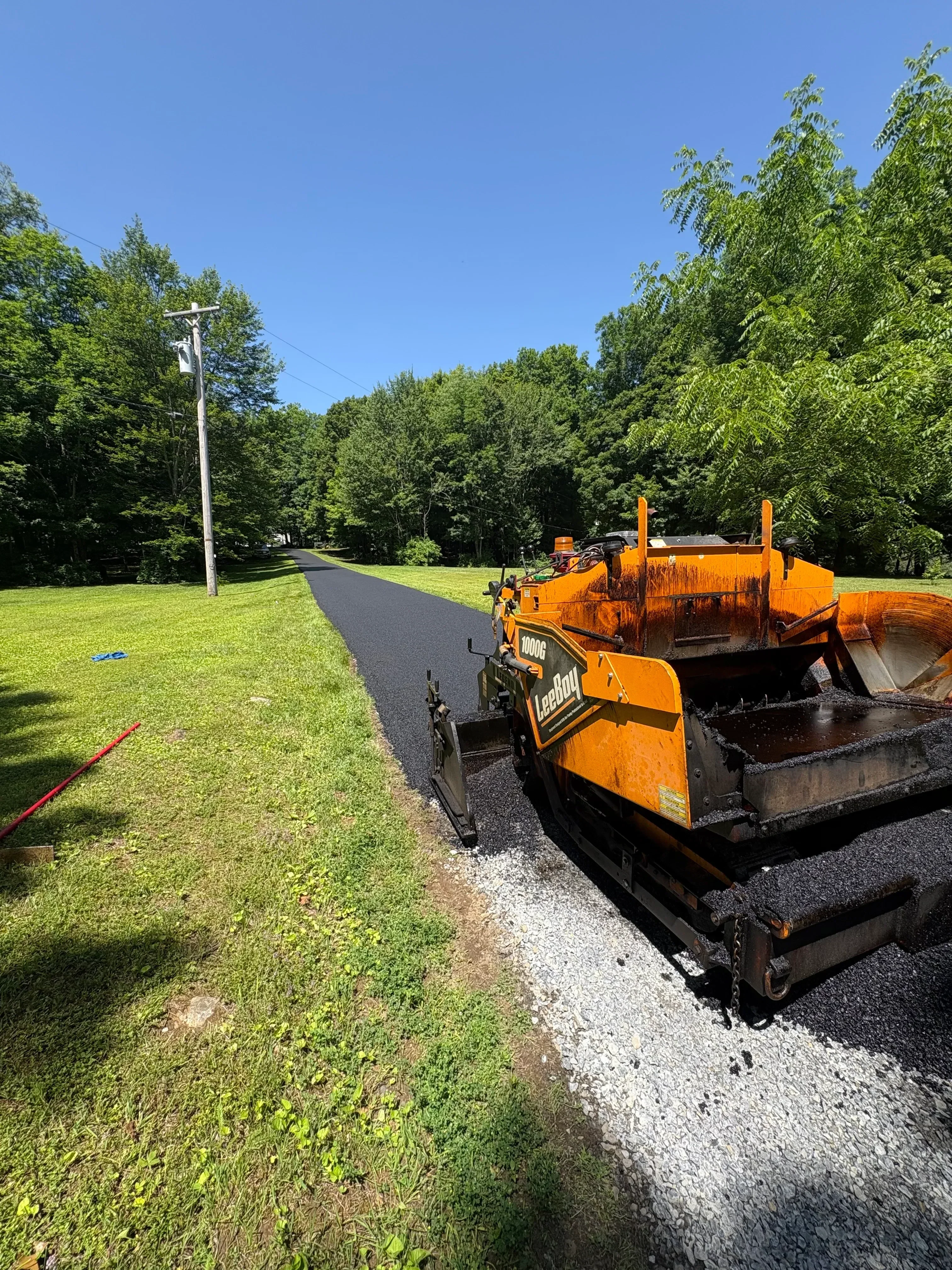 Newly paved asphalt driveway with dark surface and clean edges adjacent to green lawn
