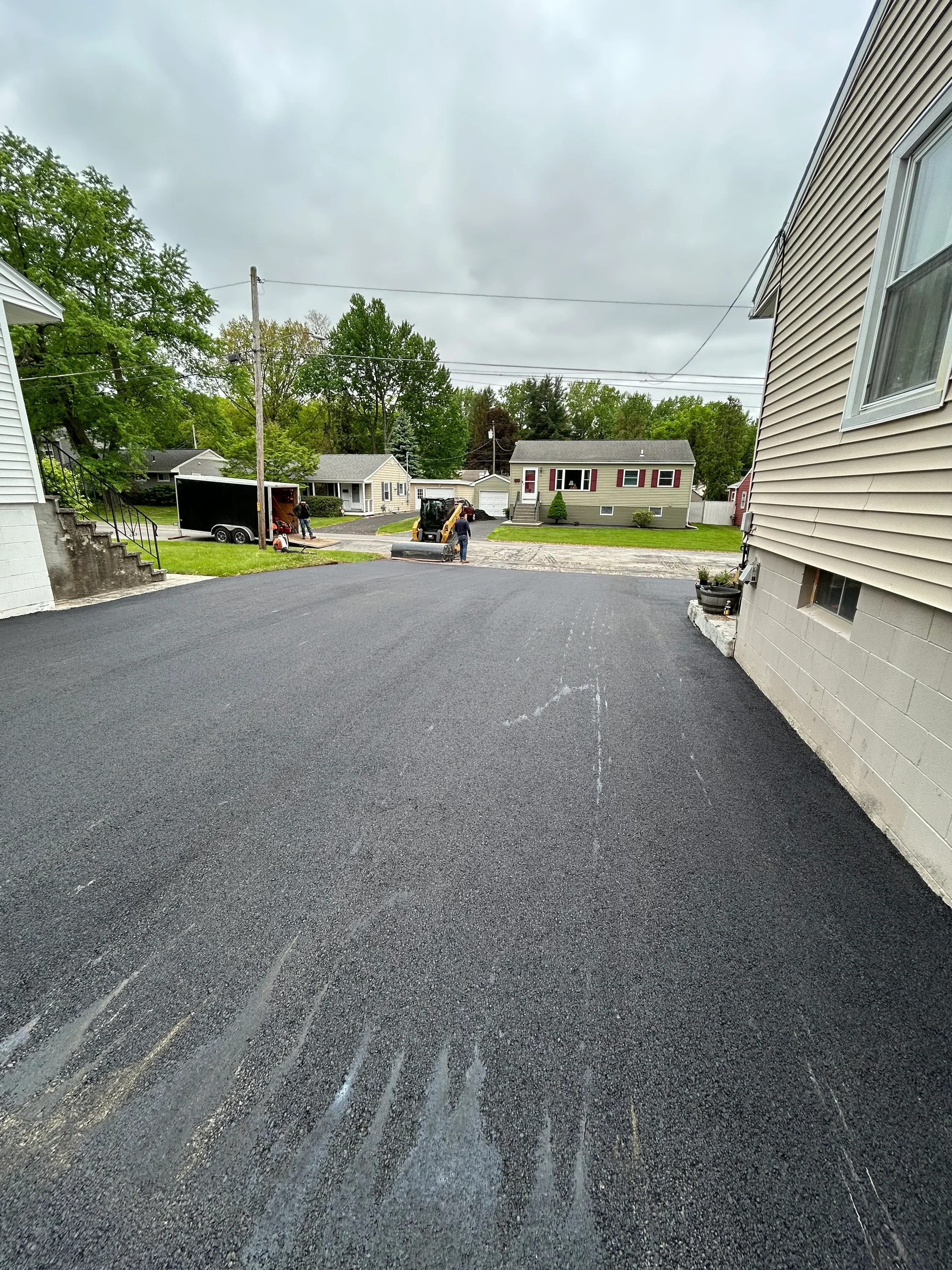Newly installed dark asphalt driveway with compacted surface leading to residential home