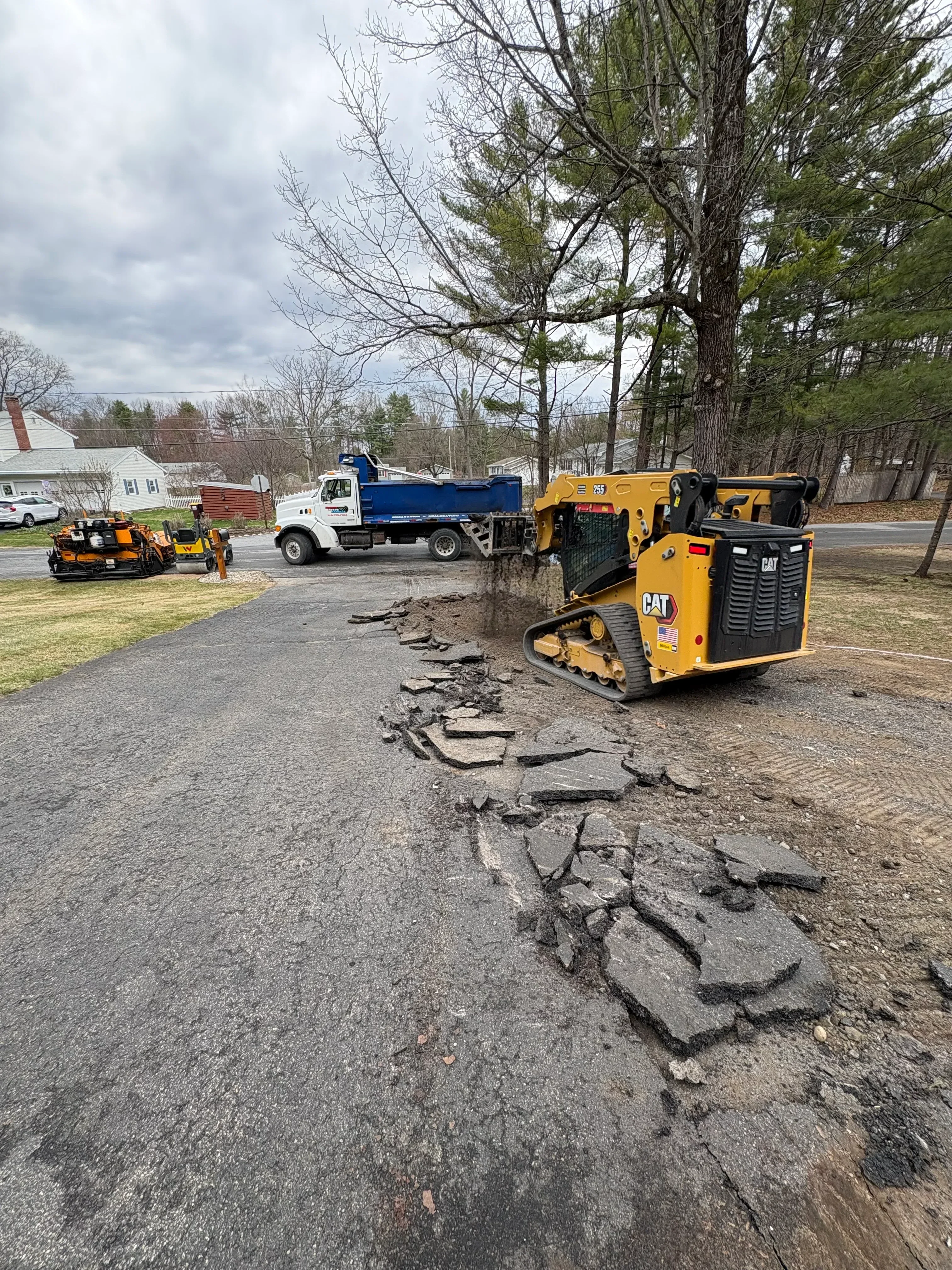 Yellow vibratory compactor and trucks on cracked asphalt surface during removal project
