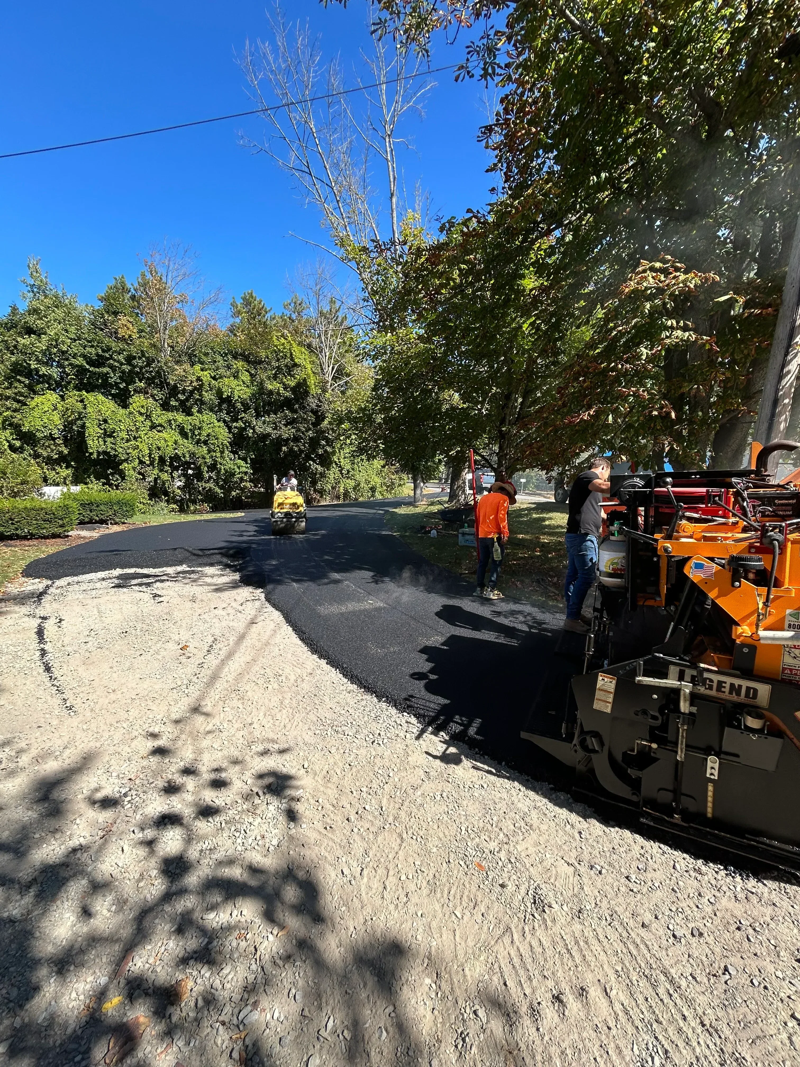 Orange paving equipment and crew installing fresh black asphalt on residential driveway