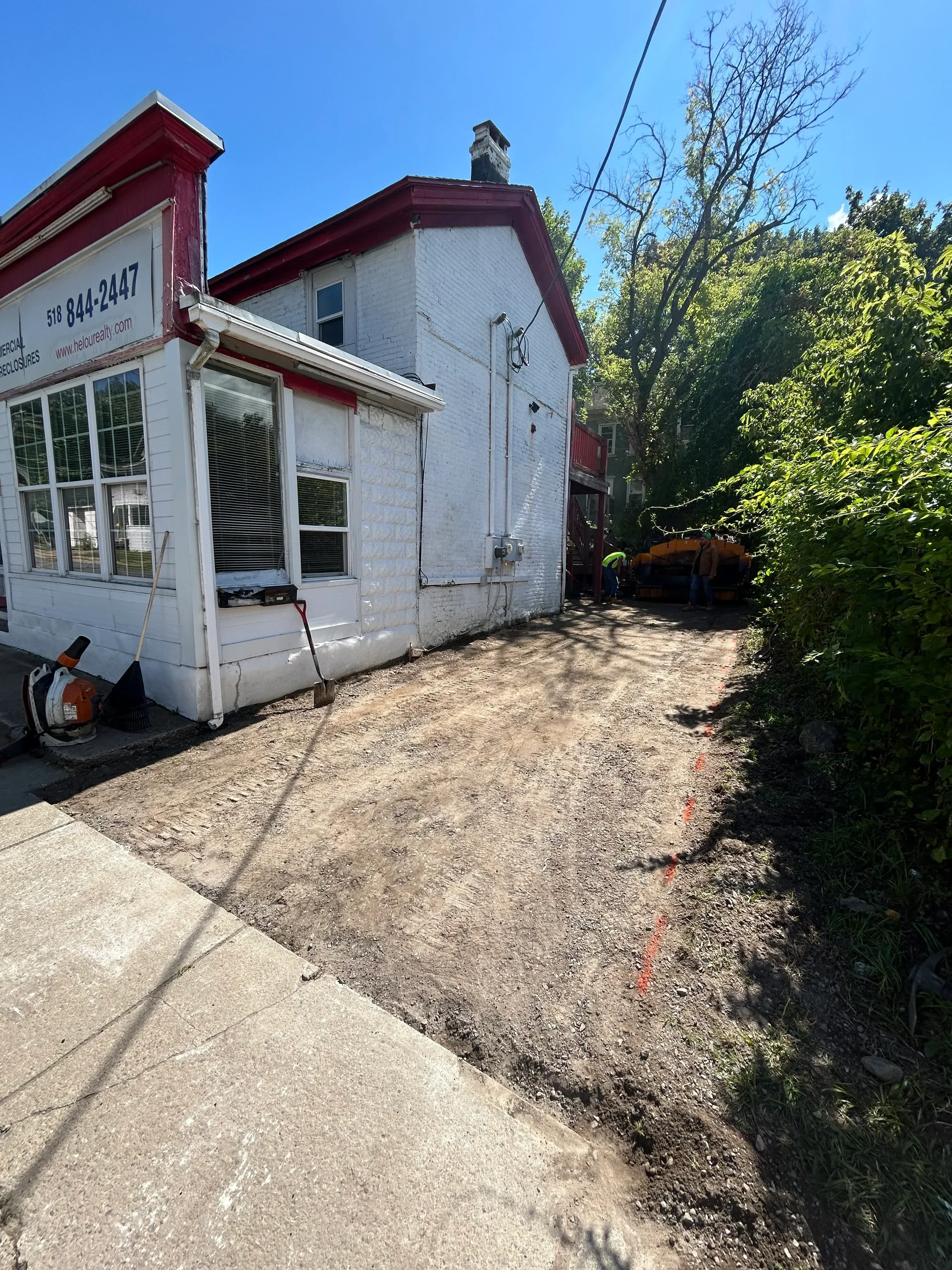 Newly paved asphalt driveway with compacted surface next to residential building with red trim