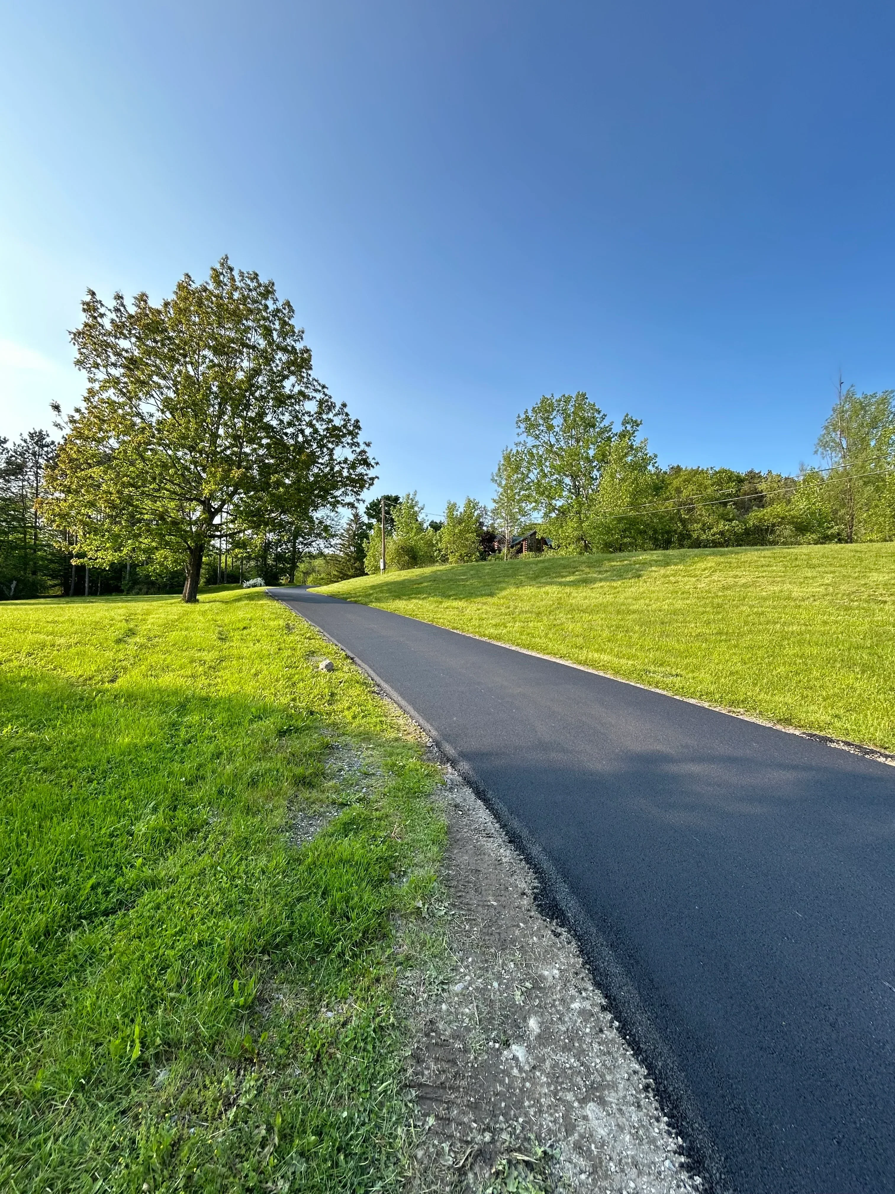 Asphalt driveway with gravel edge bordering green lawn and landscaping