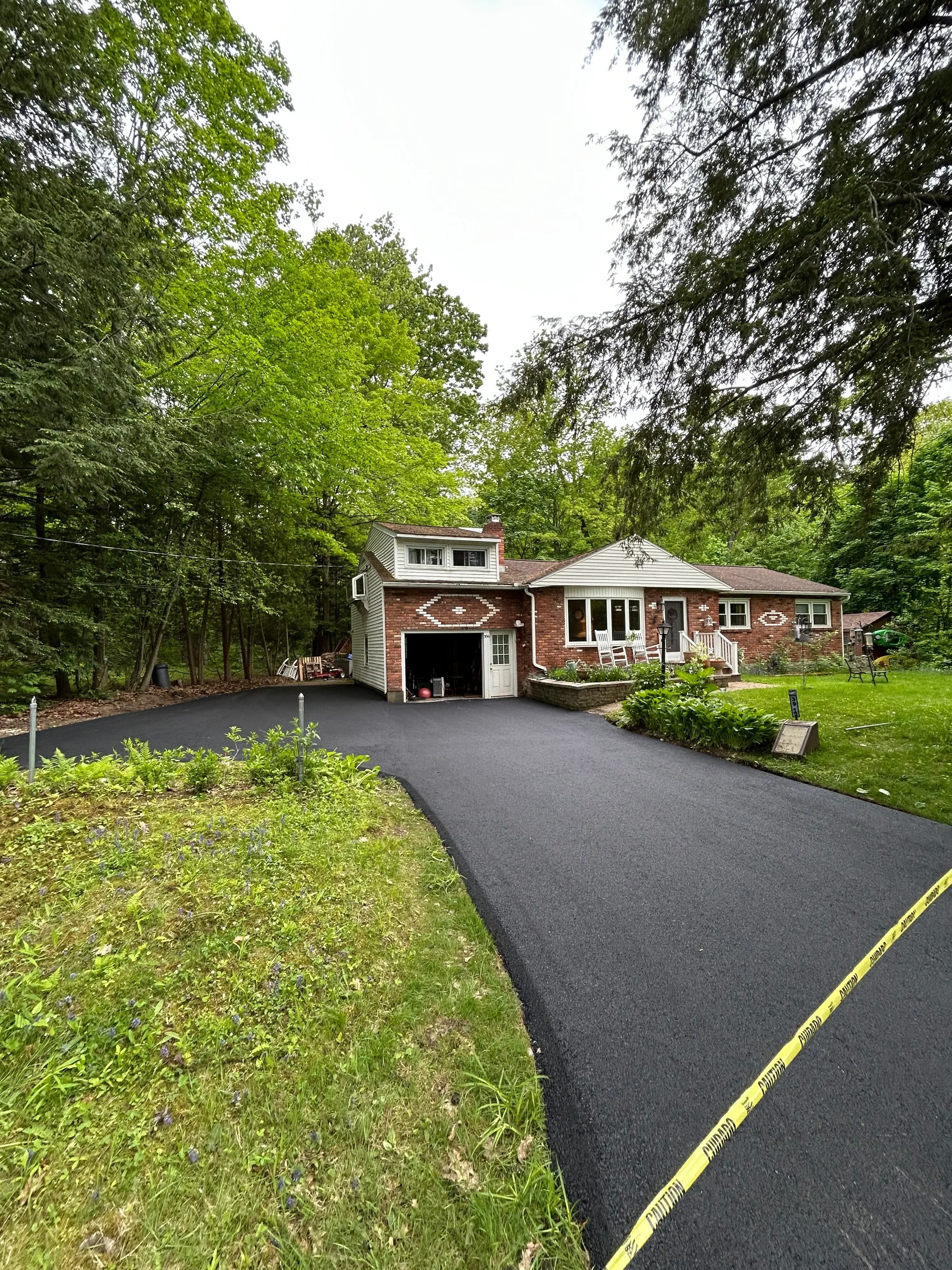 New asphalt driveway with yellow striping alongside brick home and mature landscaping