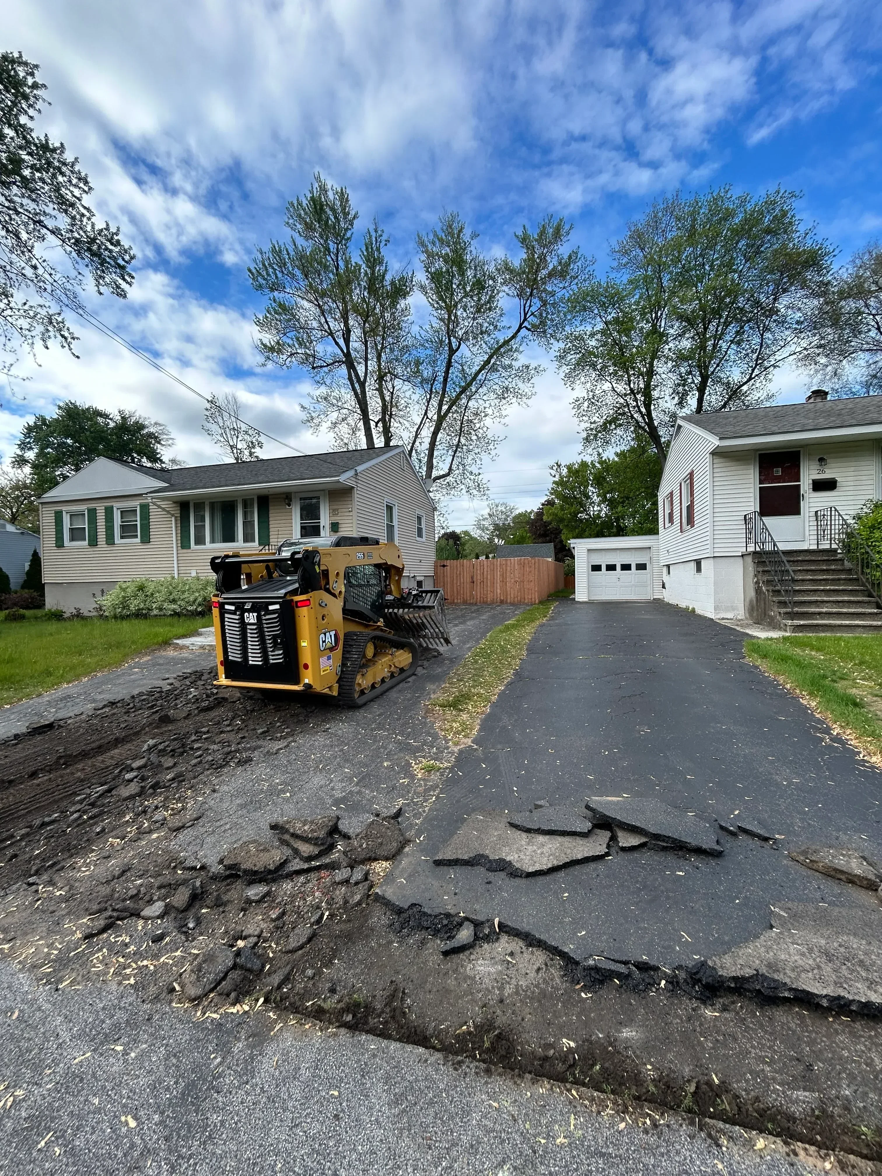Skid steer loader on residential asphalt driveway with crack repairs and fresh overlay