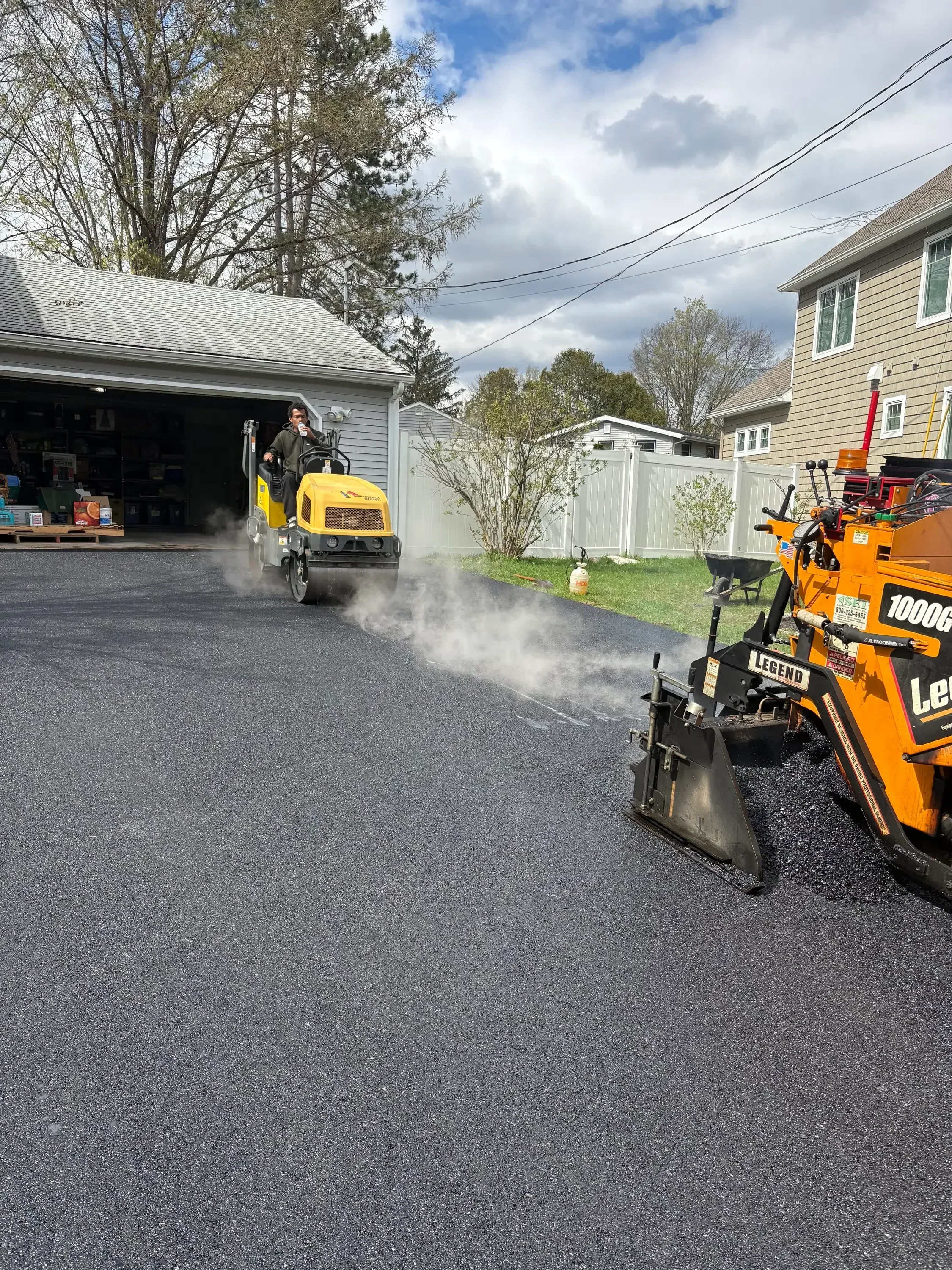 Yellow pressure washing truck cleaning dark asphalt driveway with high-pressure water stream