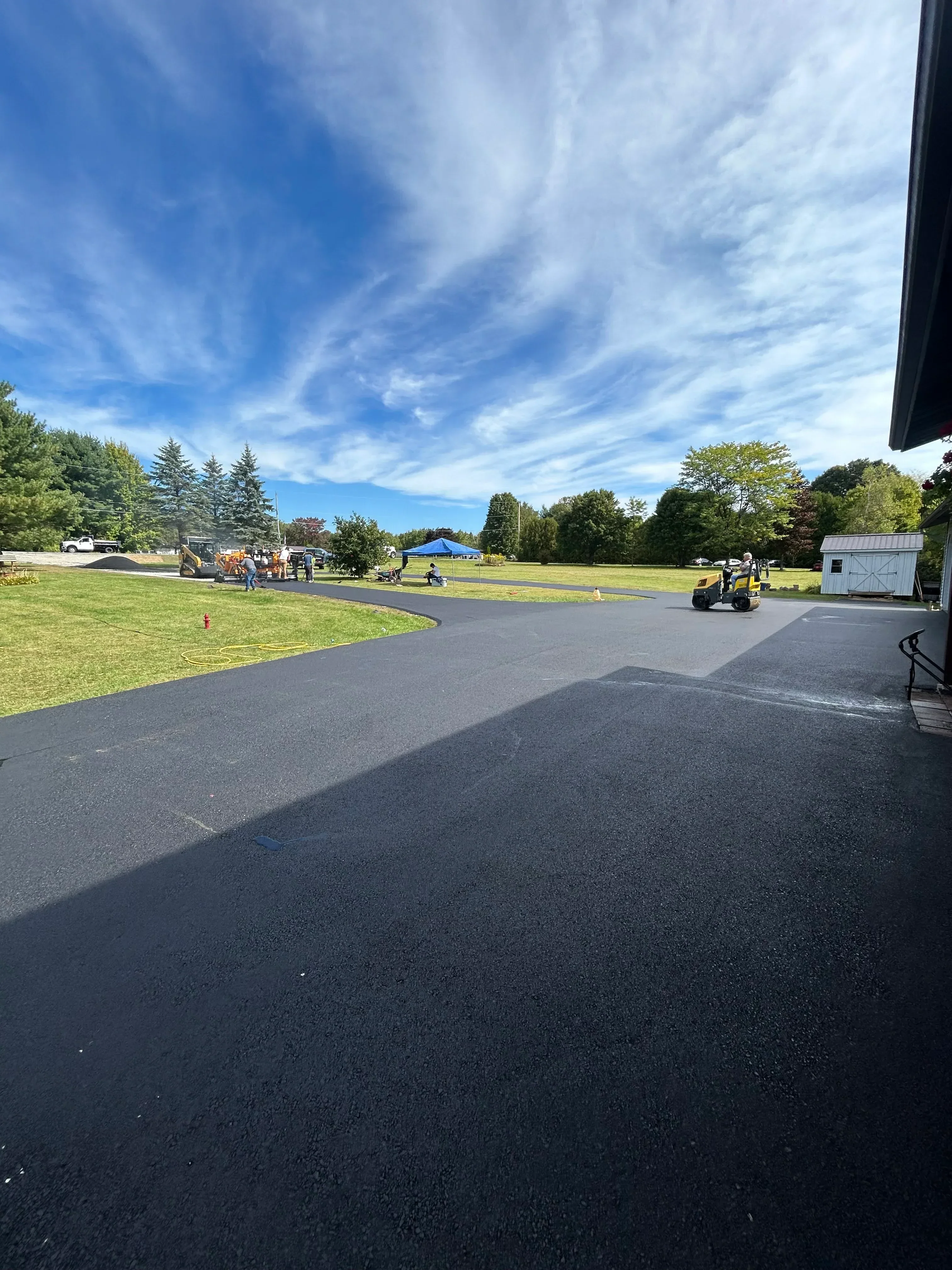 Newly installed black asphalt driveway with manicured lawn and mature landscaping