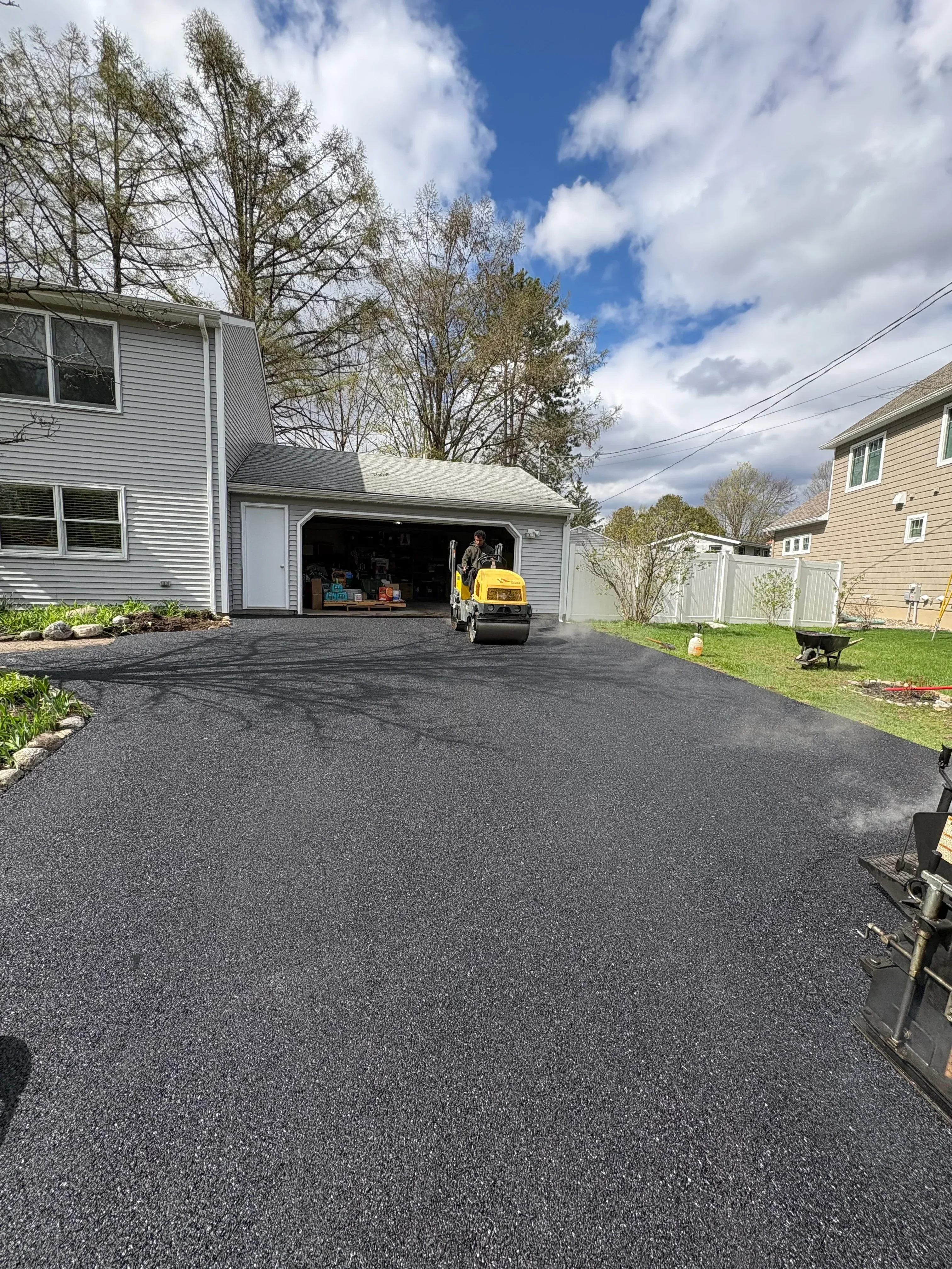 Newly installed dark asphalt driveway with compacted surface next to residential home