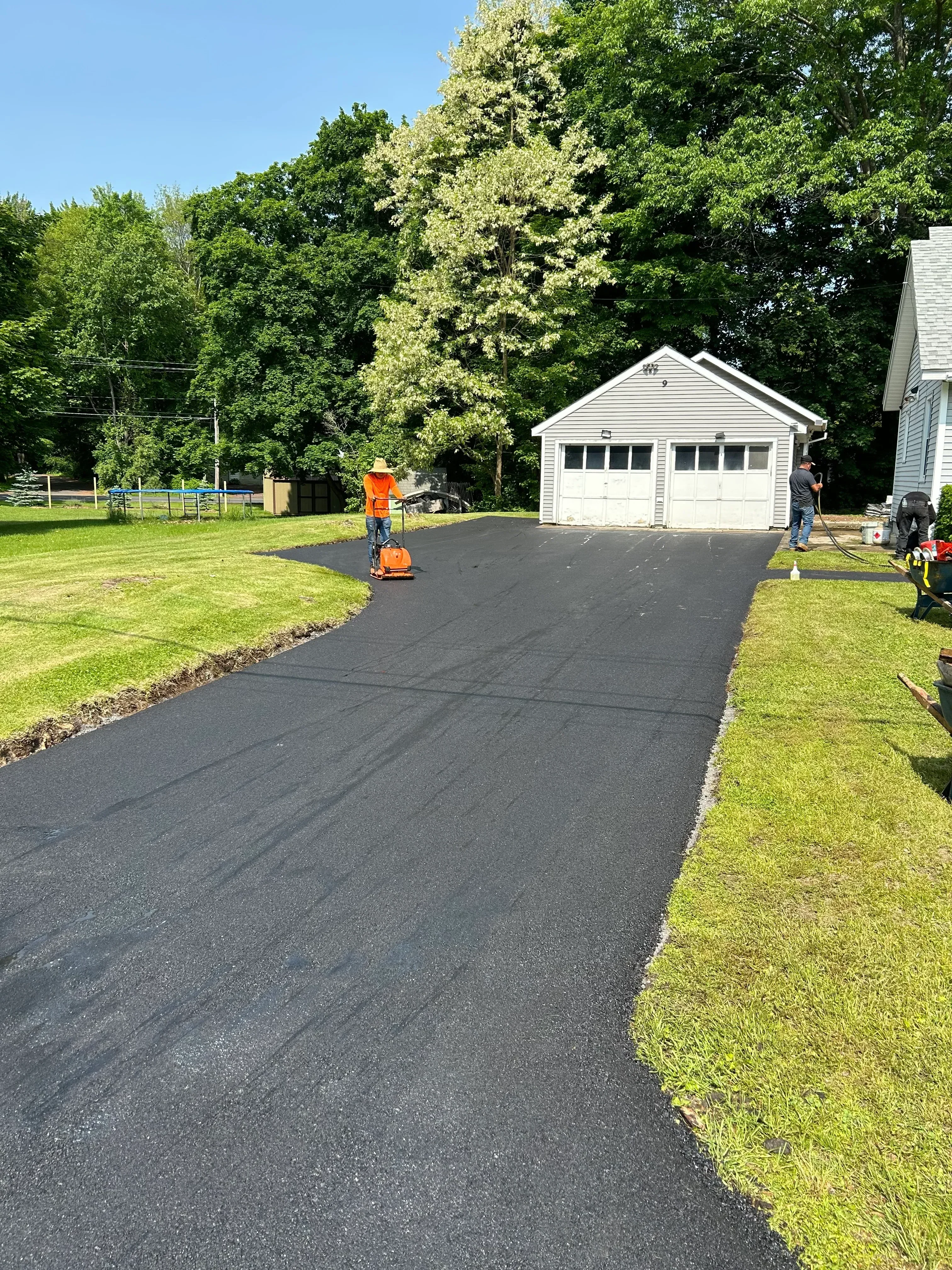 Newly installed black asphalt driveway with compaction roller and residential structure