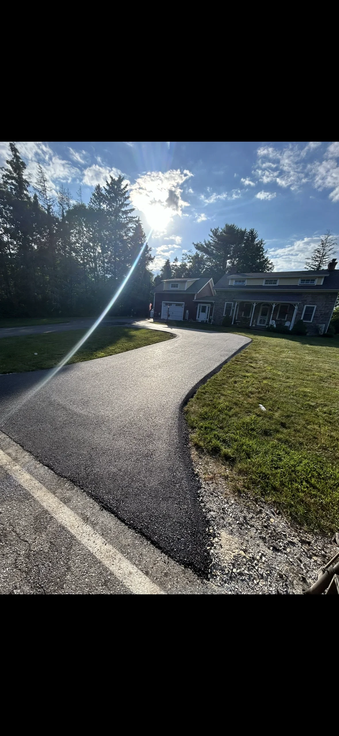 Curved asphalt driveway with gravel borders leading to residential home