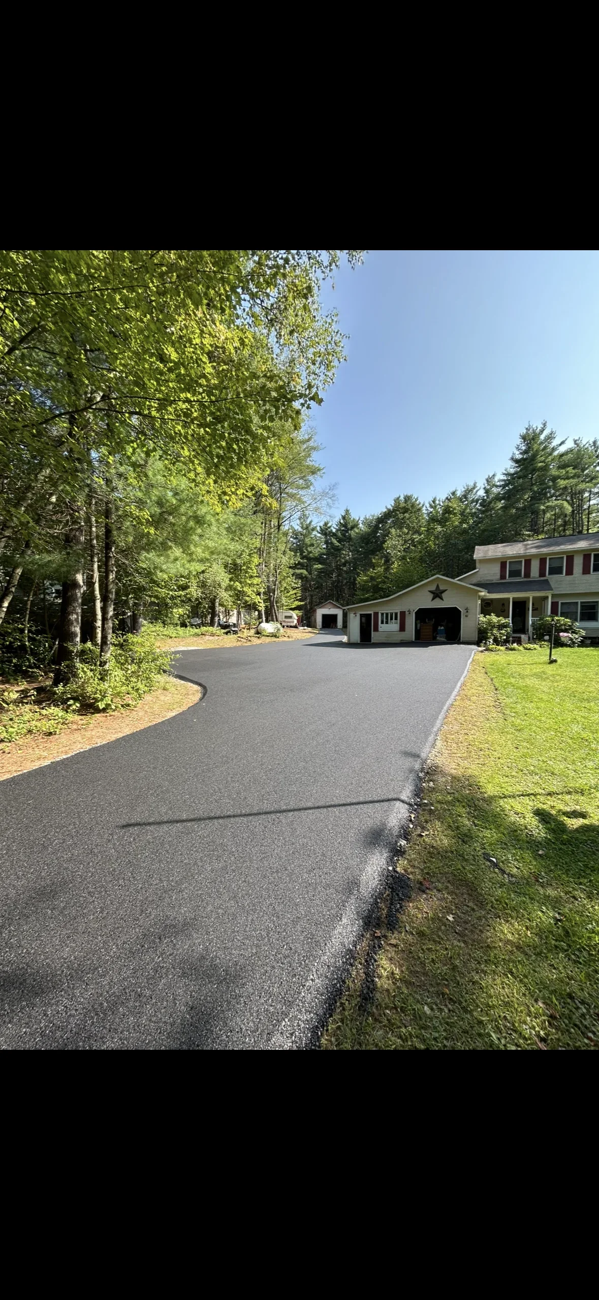 Newly paved asphalt driveway with curved design, mature trees, and residential home with garage