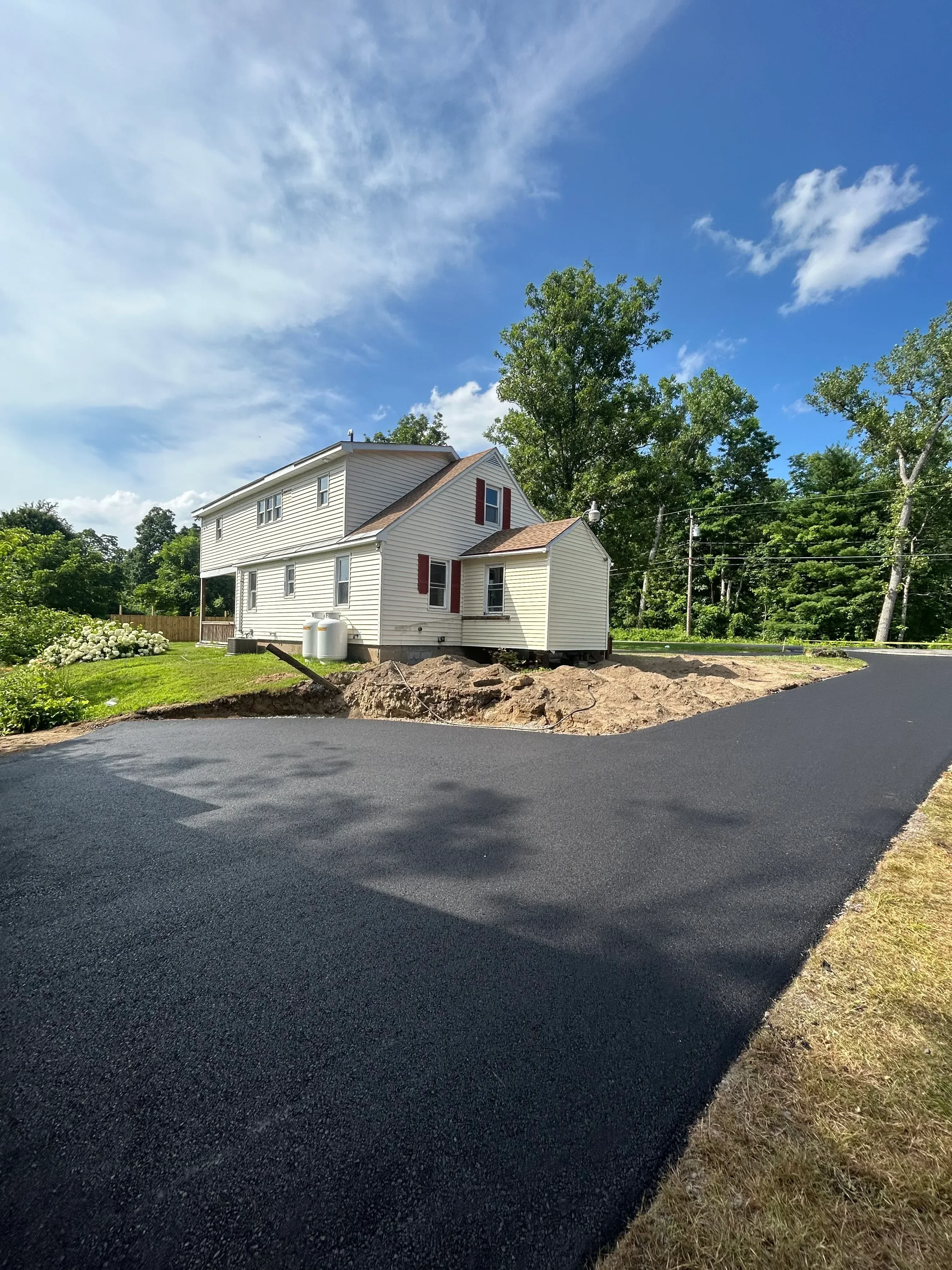 Newly installed black asphalt driveway leading to residential home with metal siding