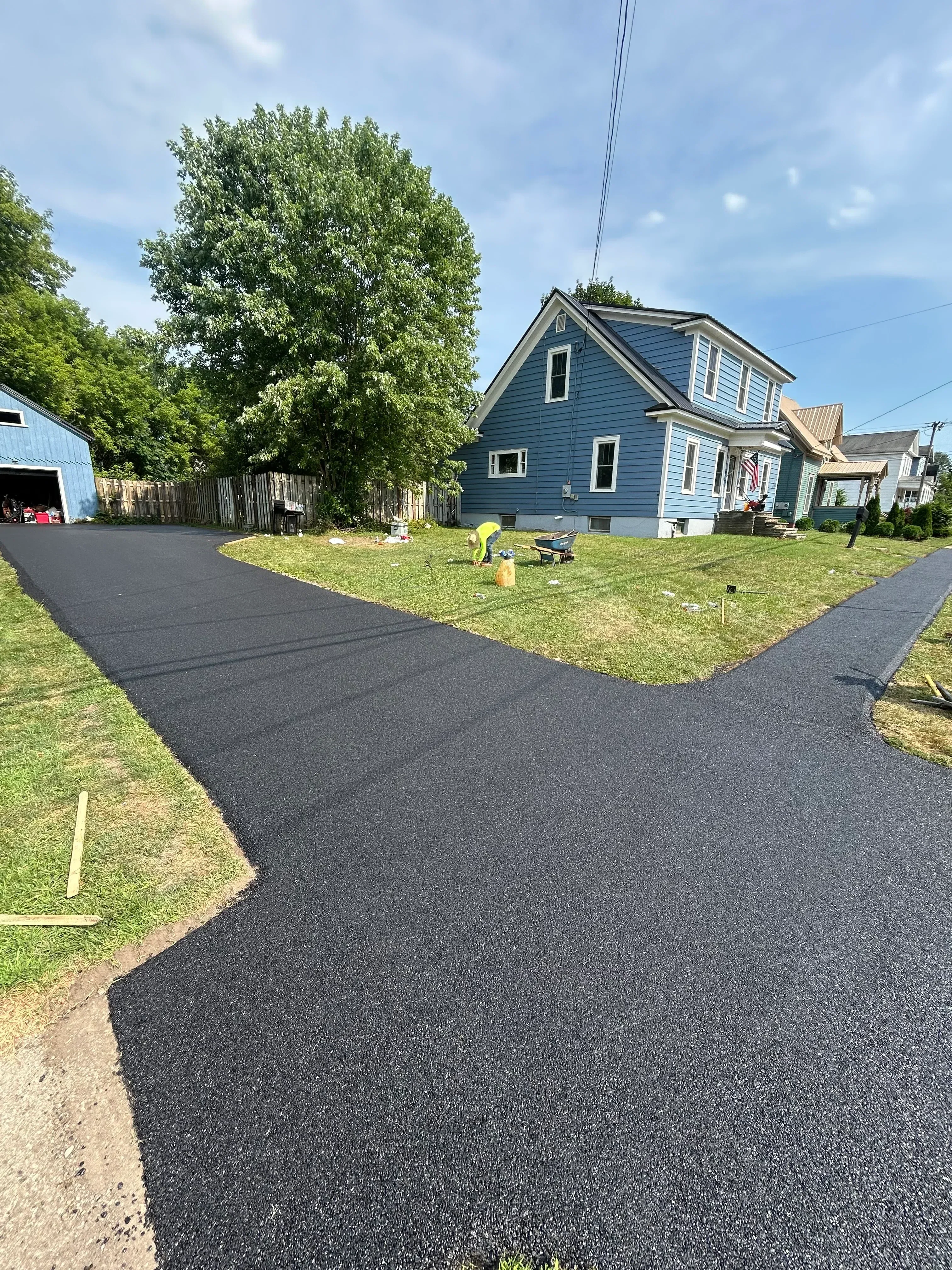New asphalt driveway installation beside residential home with metal roof and landscaping