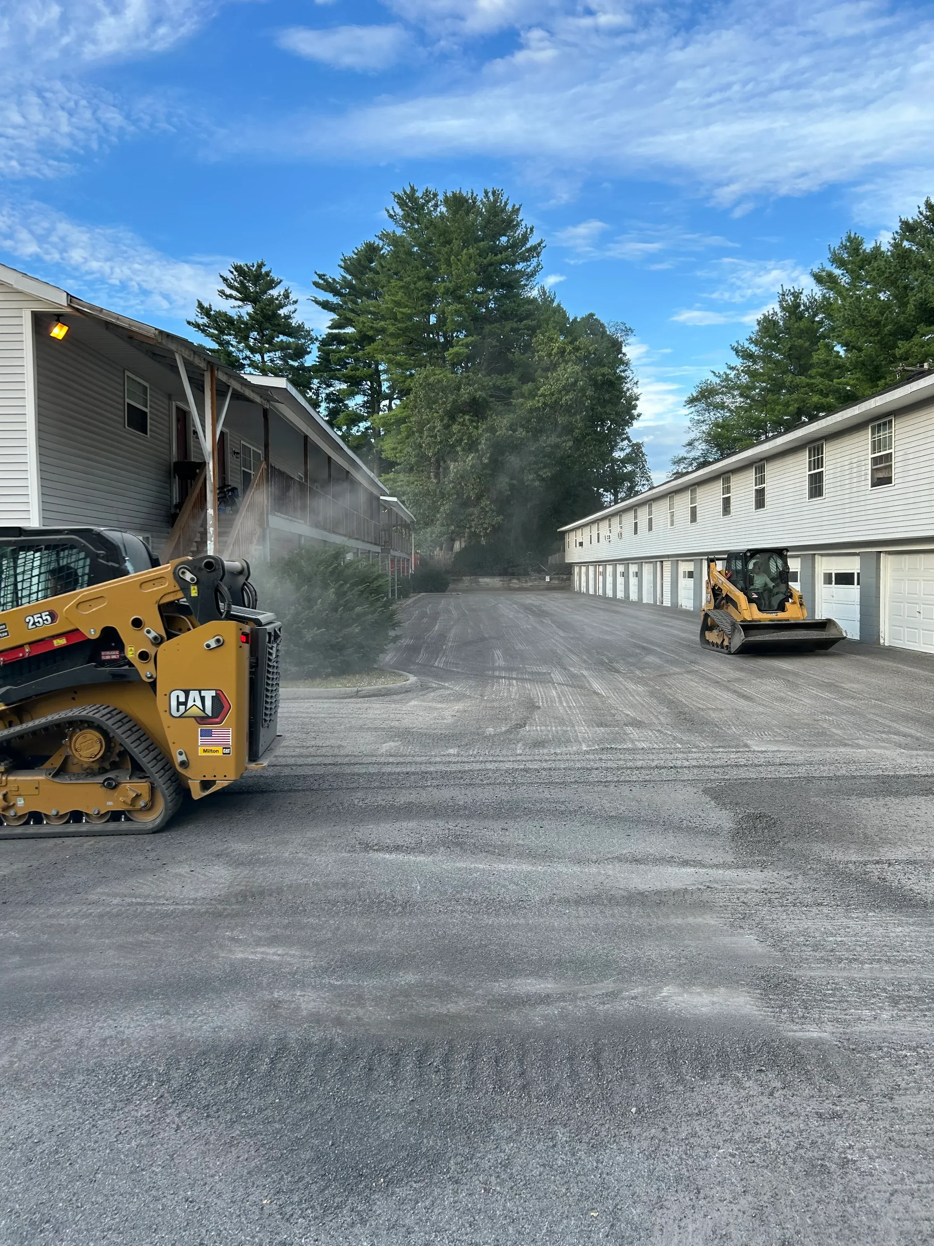 Skid steer loader compacting fresh asphalt on residential driveway