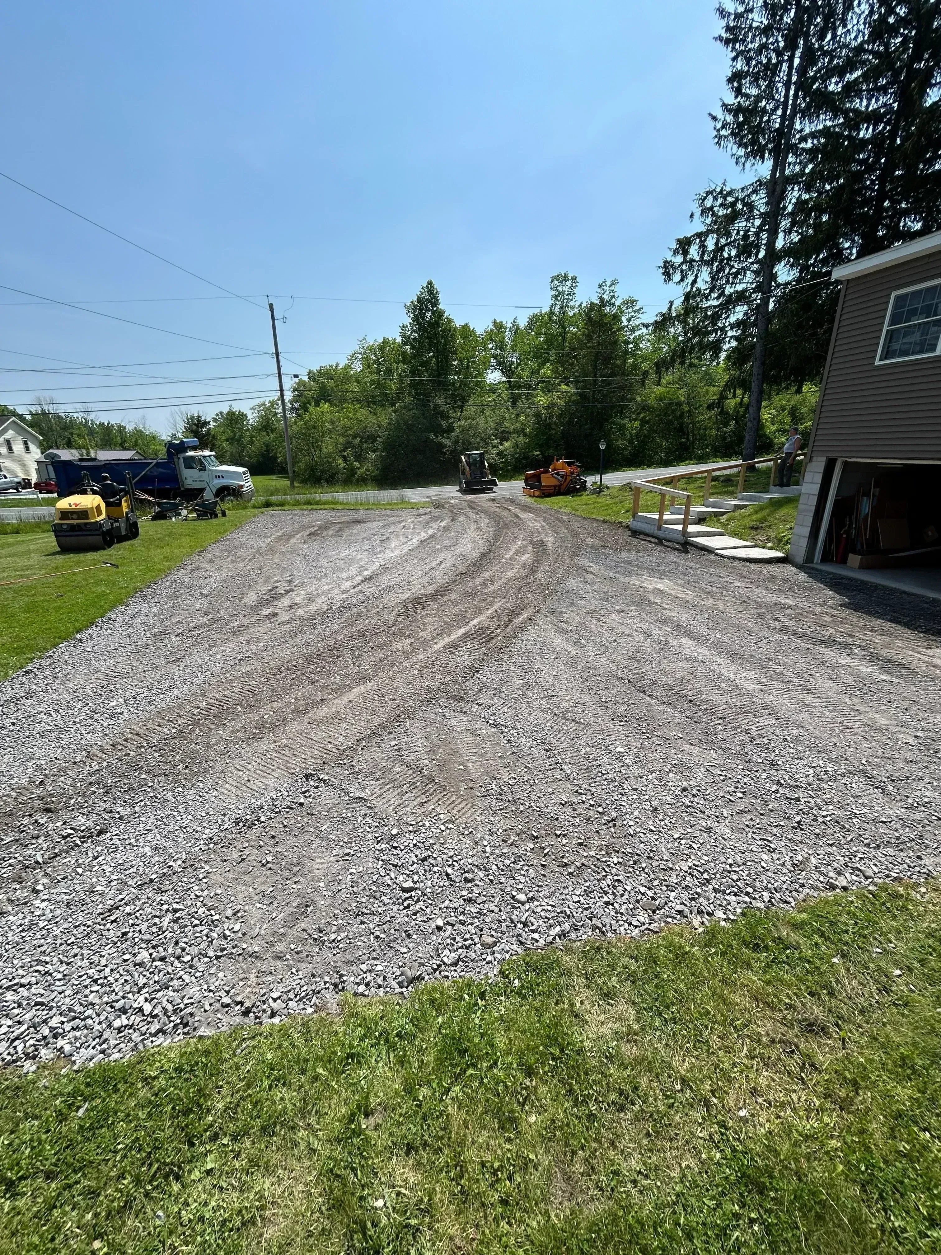 Freshly paved asphalt driveway with compaction marks and gravel base, bordered by green lawn