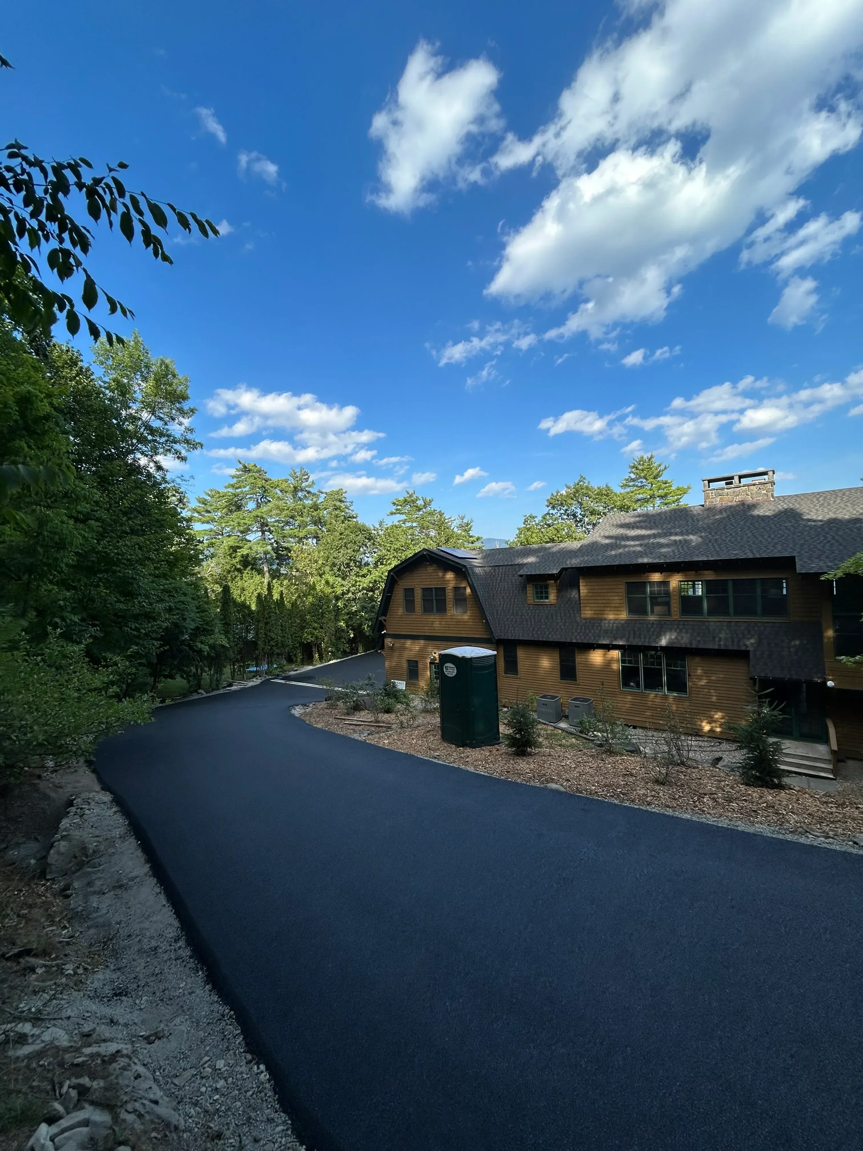 New asphalt driveway with proper grading leading to residential brick home entrance