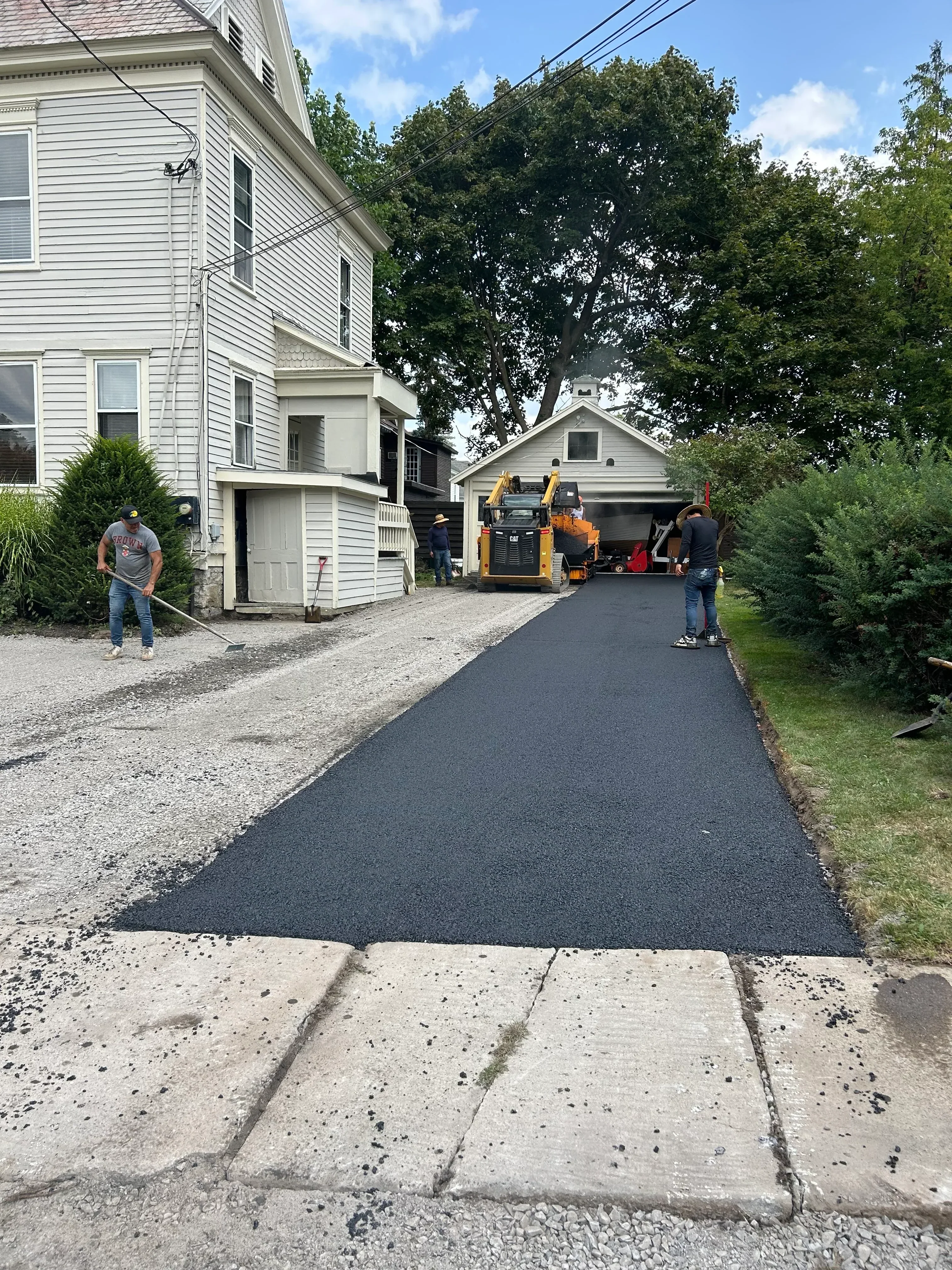Asphalt driveway installation with paving equipment and crew at residential home