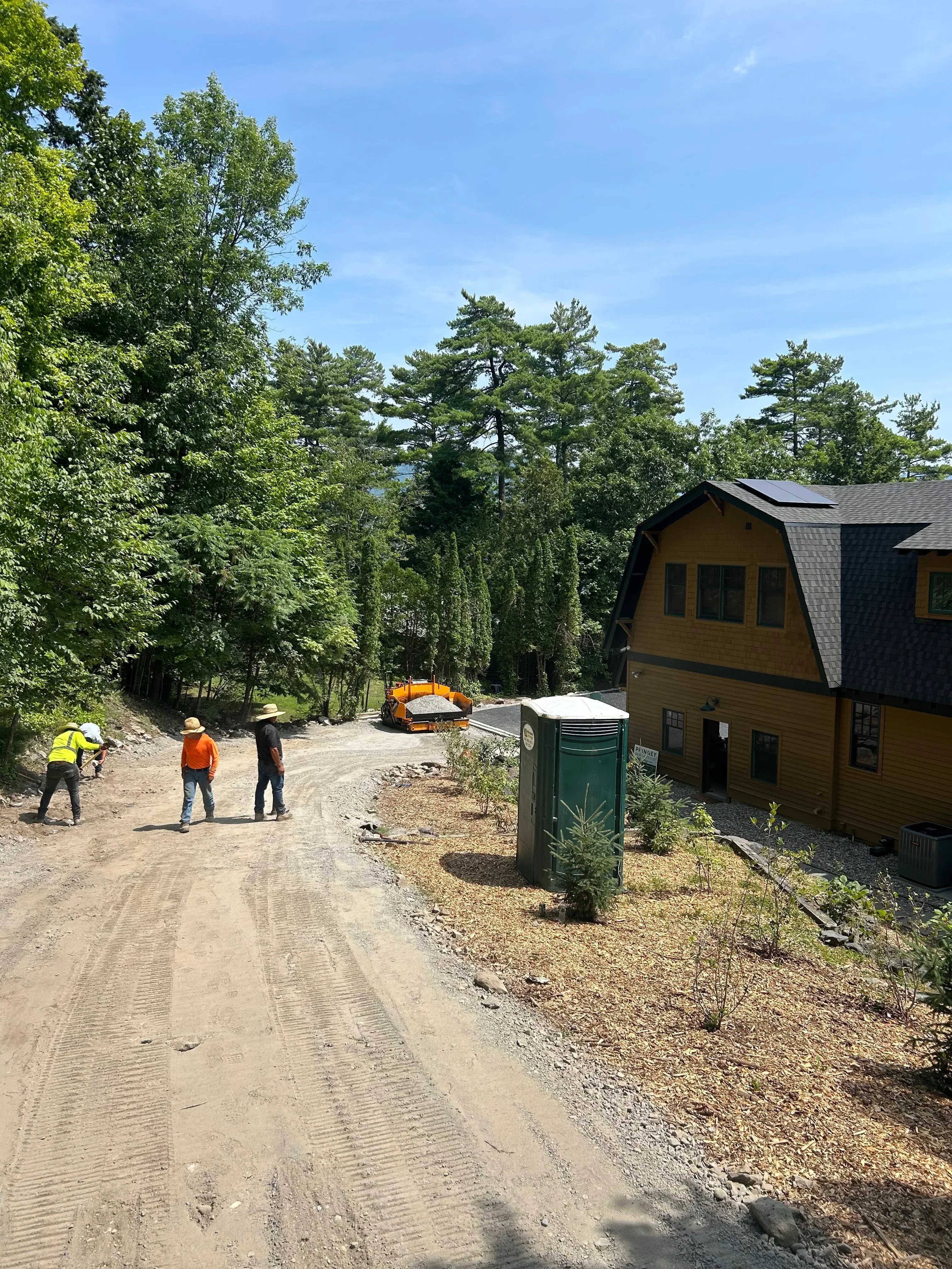 Freshly laid asphalt driveway with compaction marks, crew in safety gear on sloped residential property