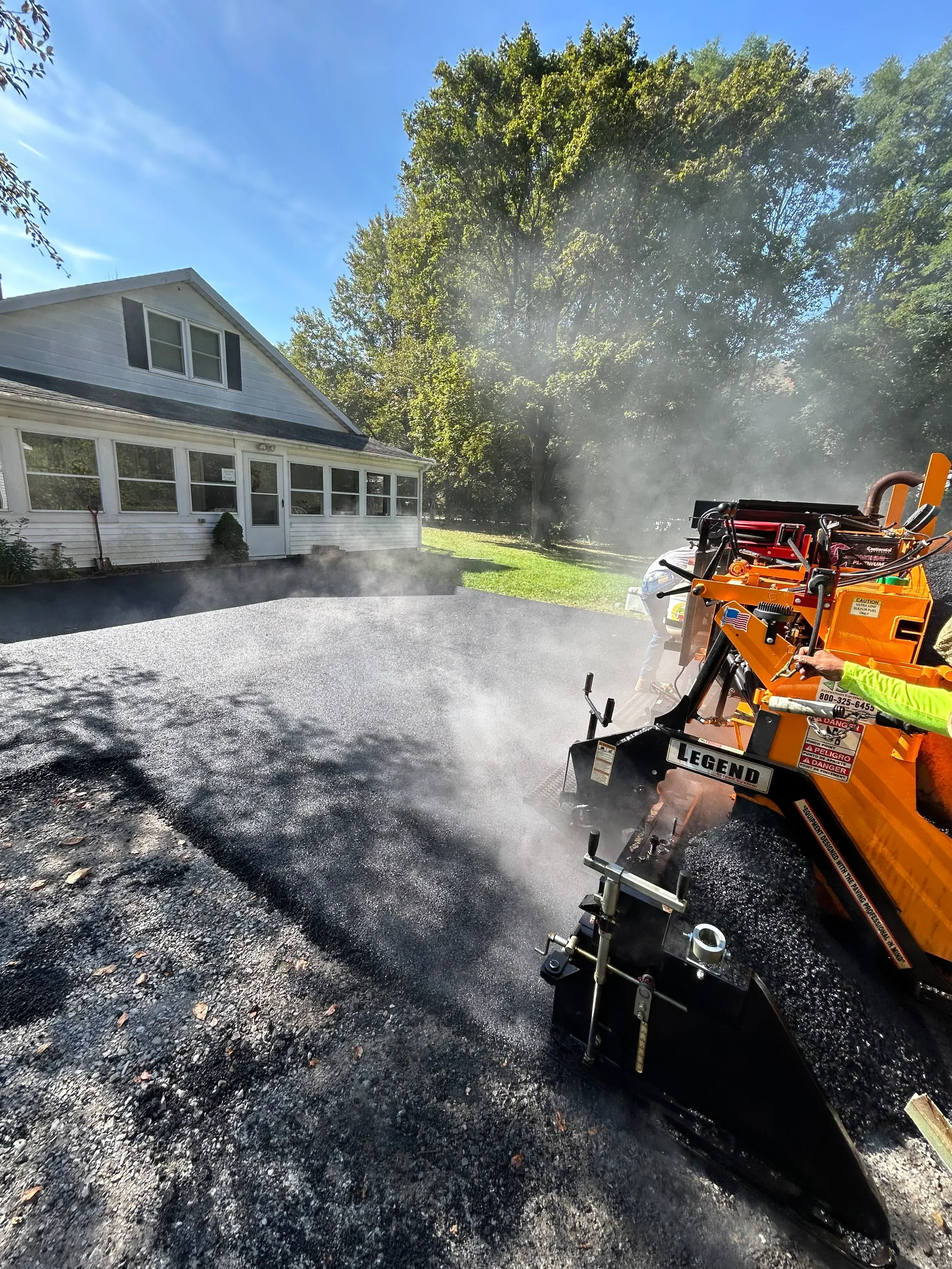 Orange asphalt milling machine removing pavement from residential driveway with dust control