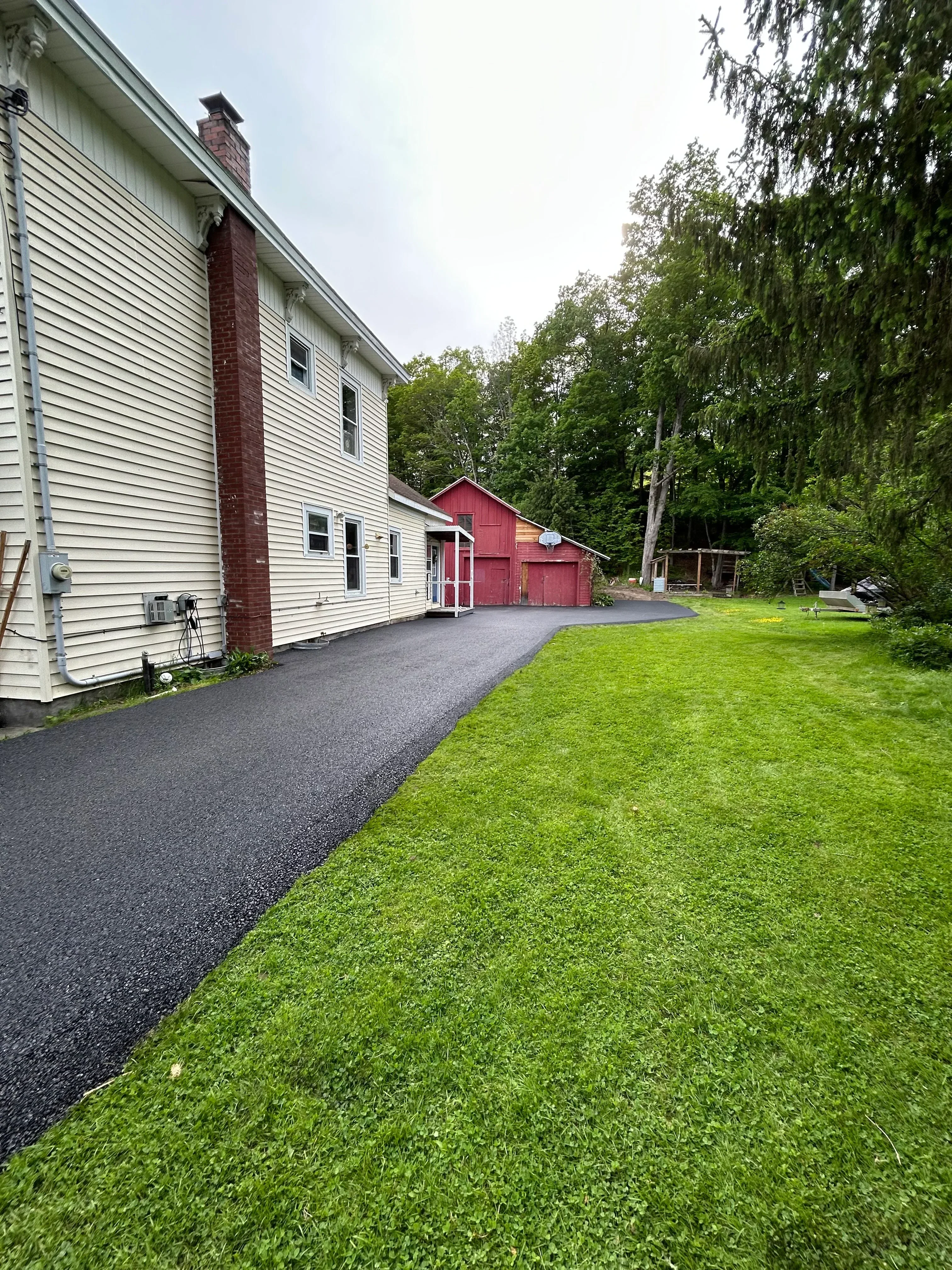 New asphalt driveway with brick house and metal roof edging