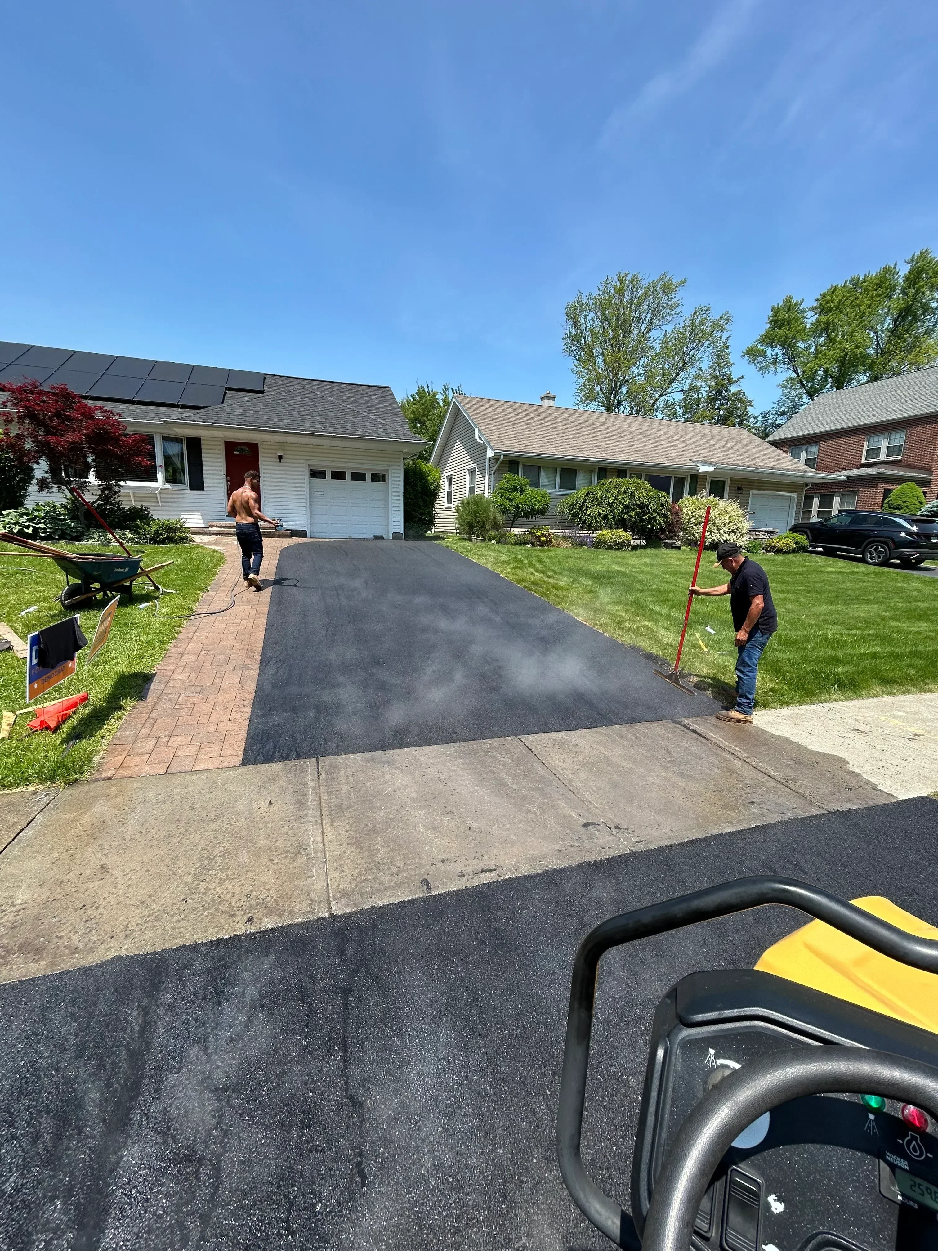 New asphalt driveway installed next to brick home with concrete walkway