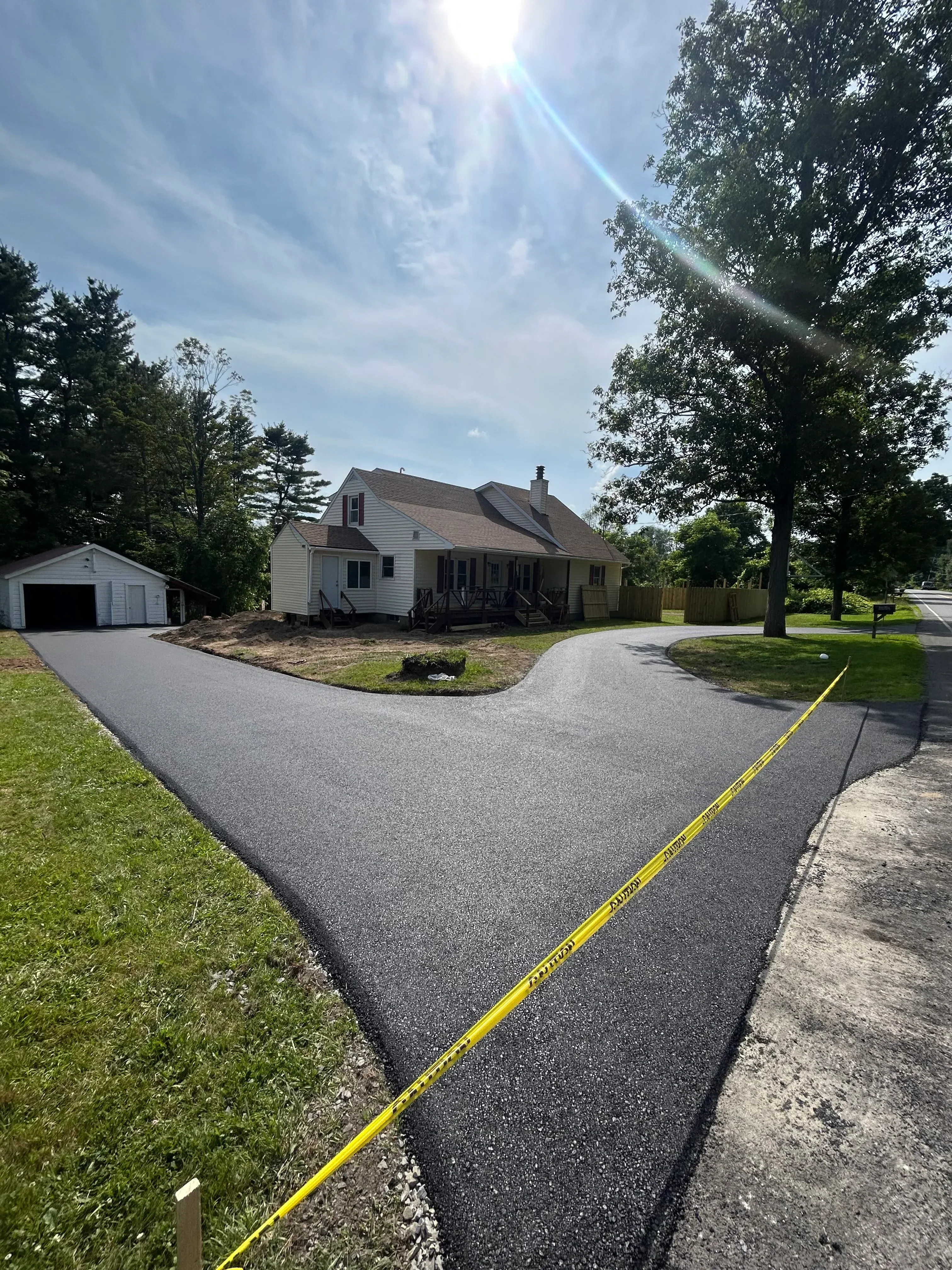 Newly installed asphalt driveway with yellow safety line and concrete edge borders